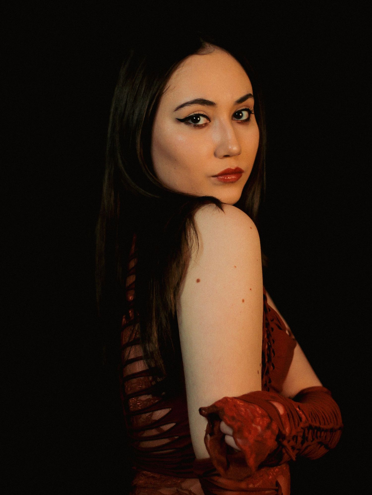 Moody portrait in burgundy dress with dramatic lighting against dark background.