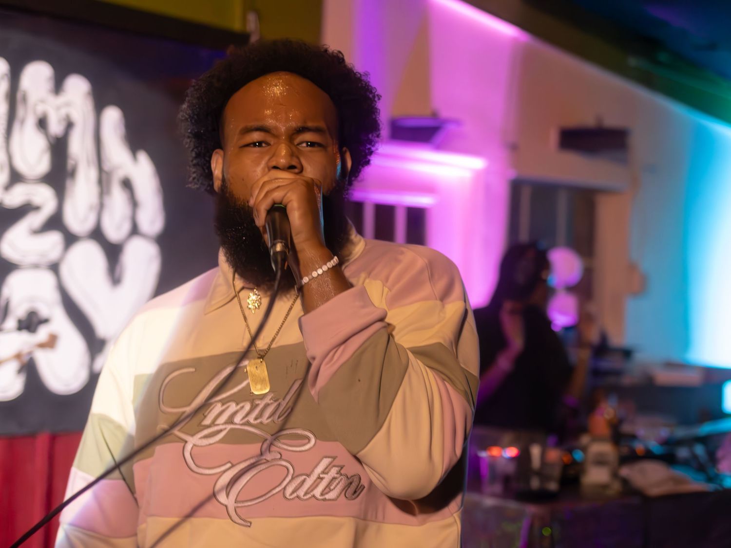 Growchild. in beige and pink sweater singing emotively on stage with dark background.