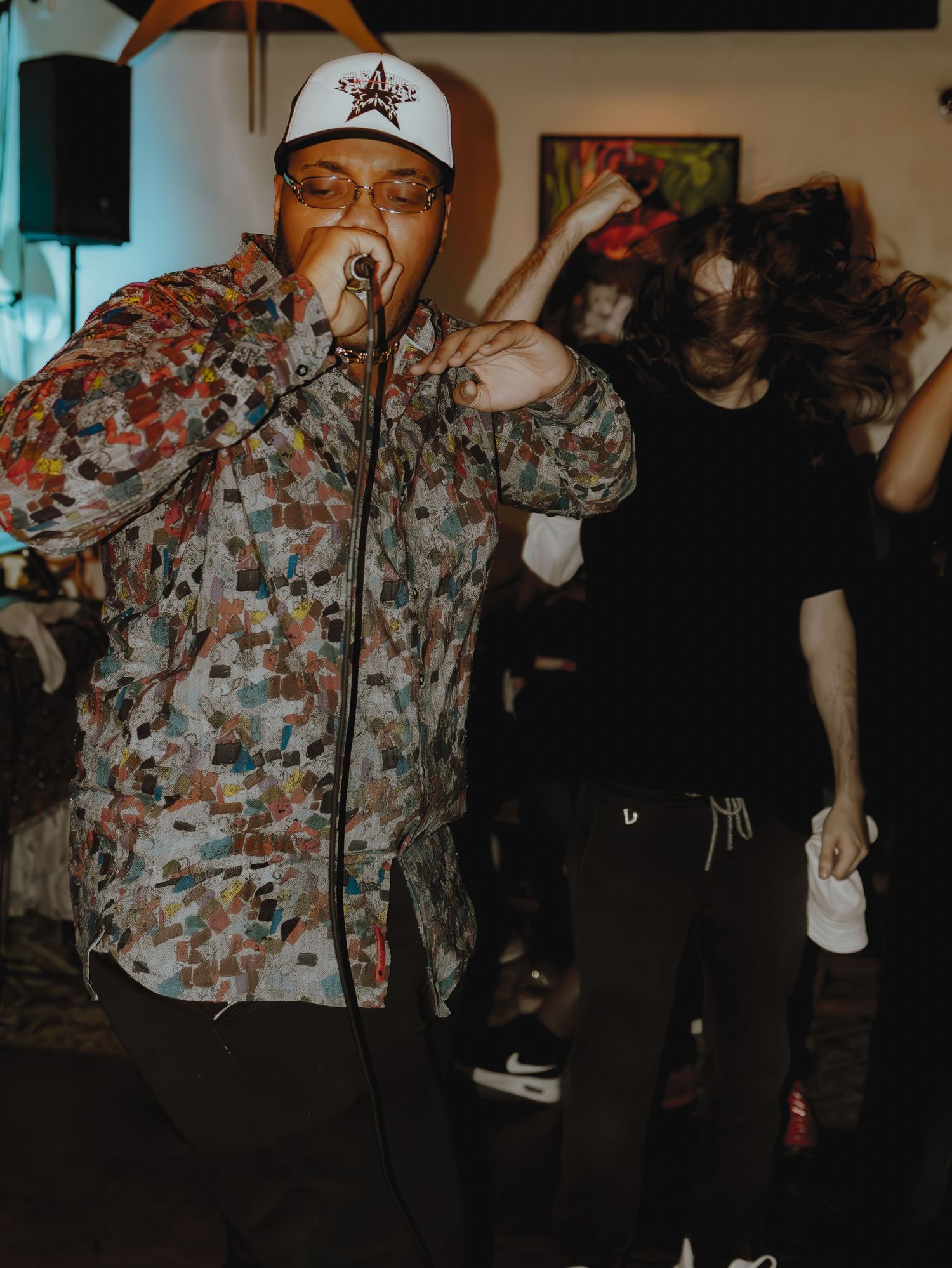A person wearing a floral print jacket performs on stage with blue ambient lighting in the background.