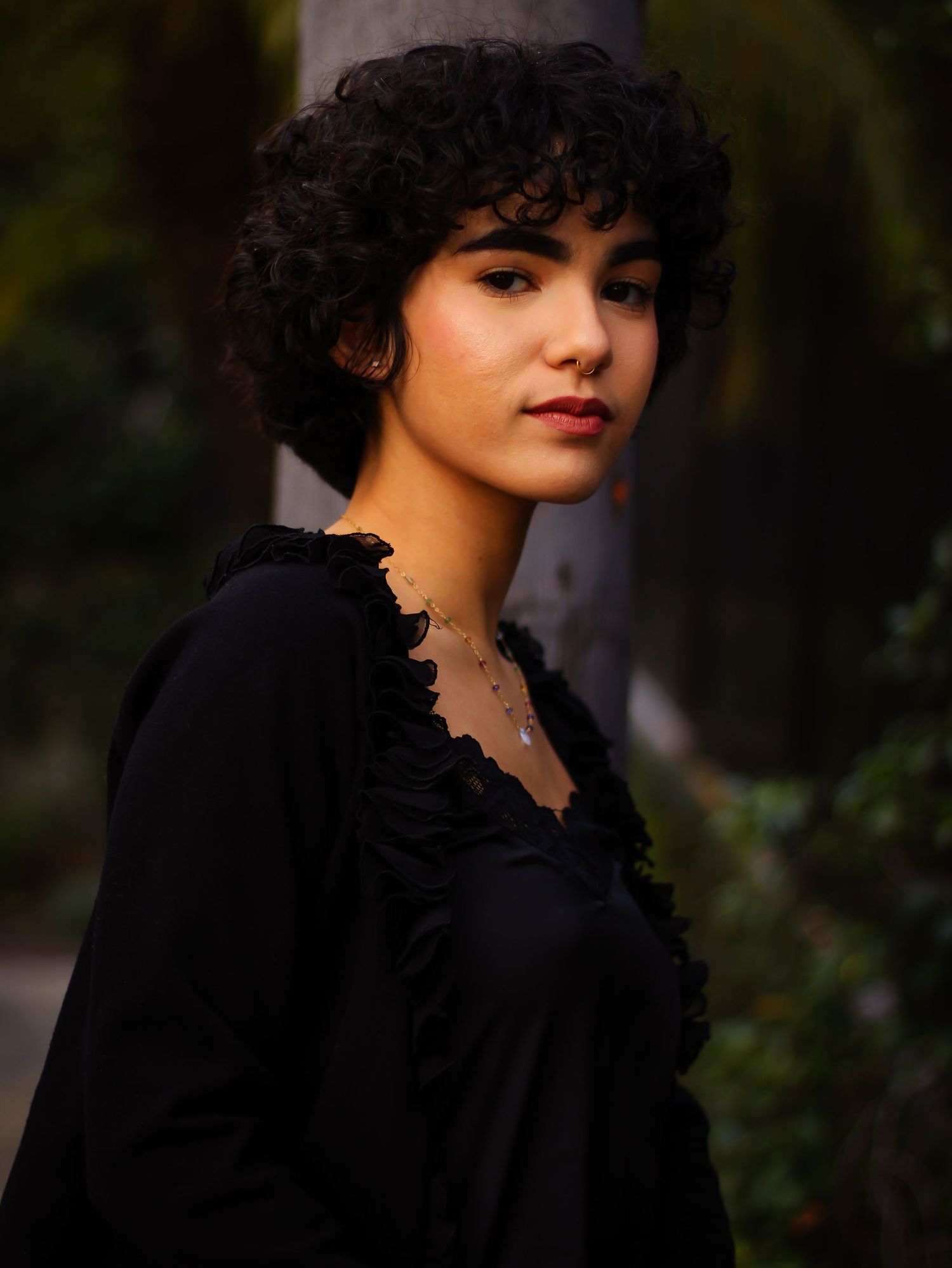 Side profile portrait in black ruffled dress against natural backdrop.