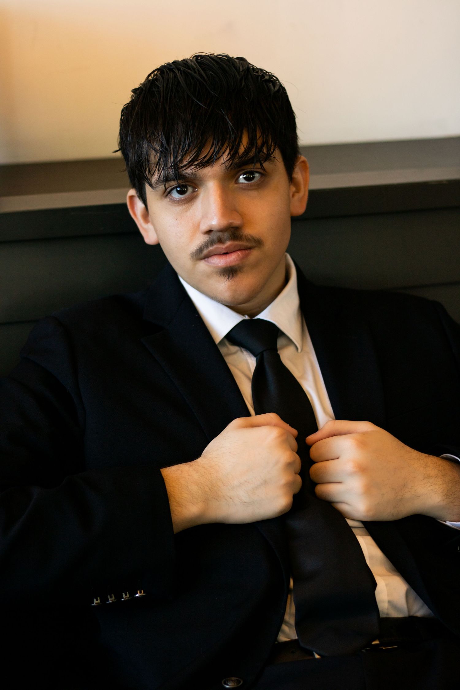 Professional portrait of person in black suit adjusting their tie.