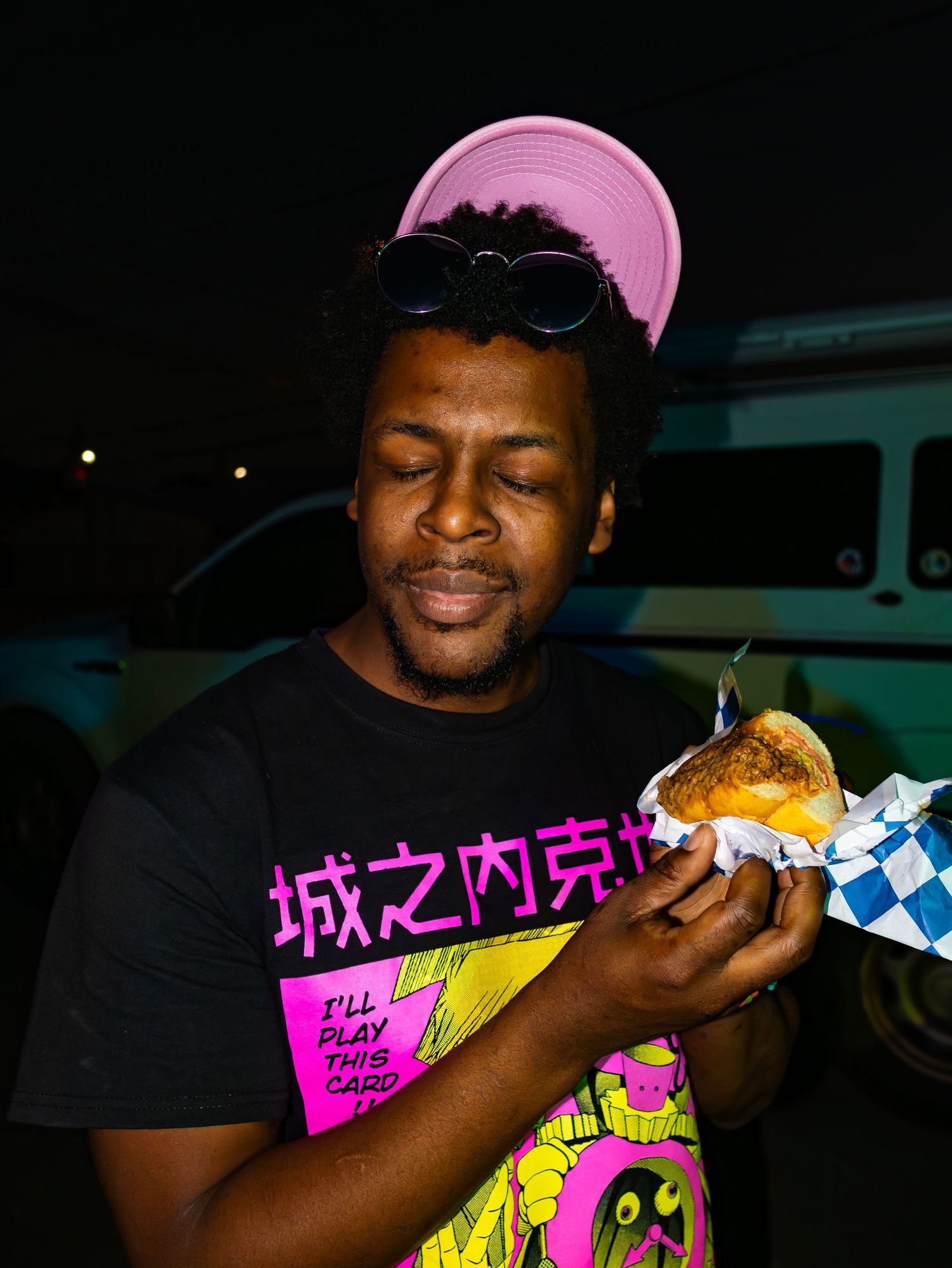Person in pink cap enjoying food at a nighttime event.