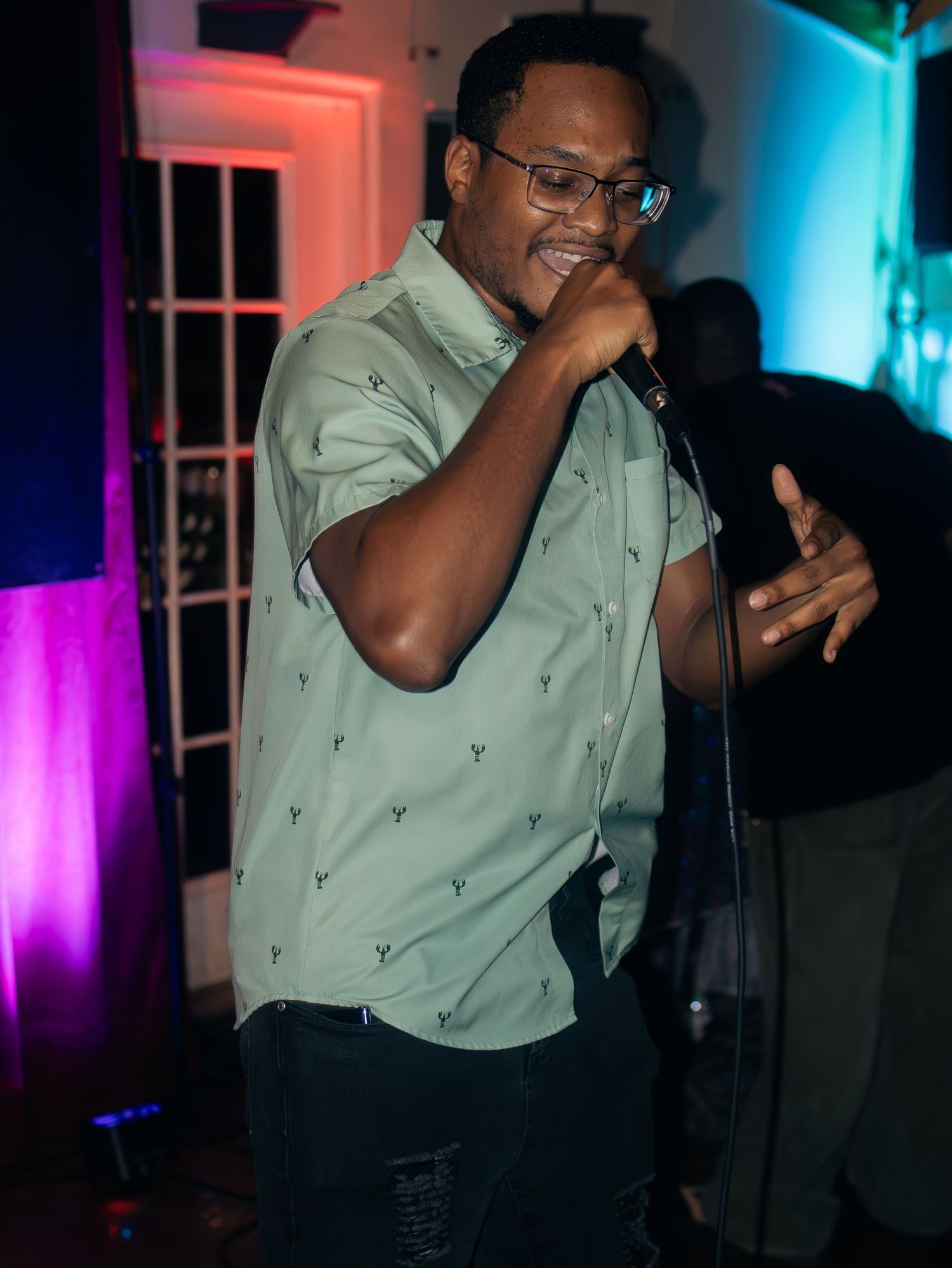 Performer in mint green button-up shirt sings emotively into microphone under theatrical lighting.