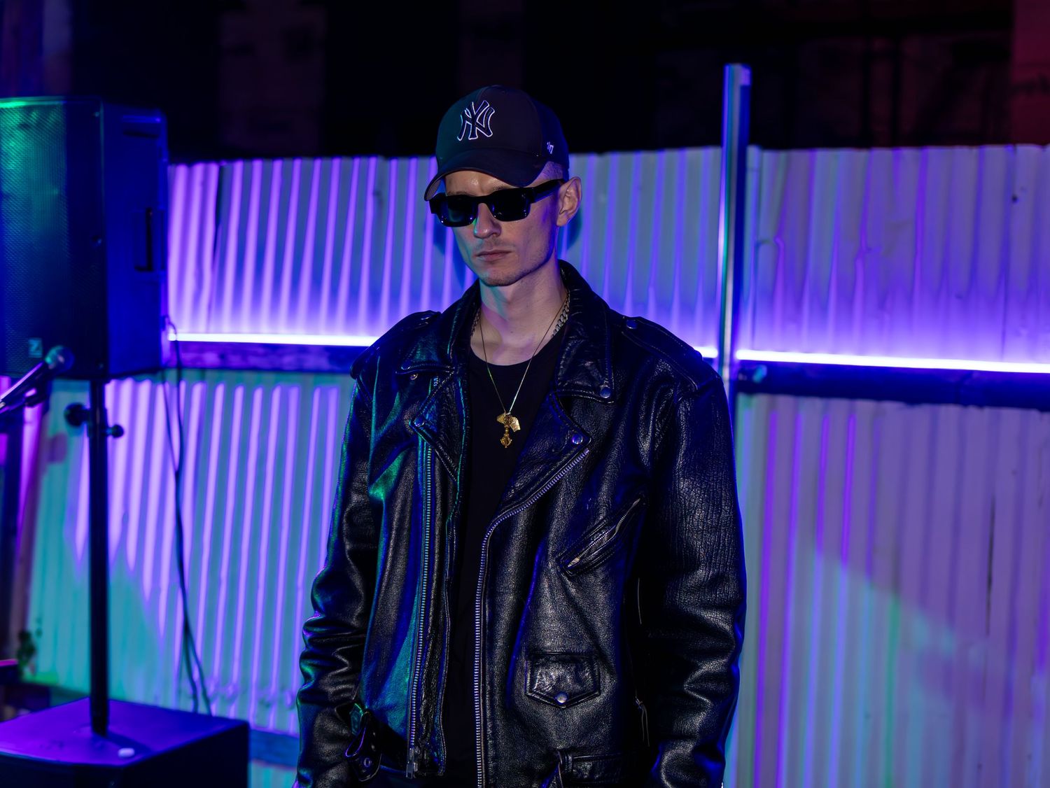 Artist in black jacket and cap performing against illuminated backdrop.