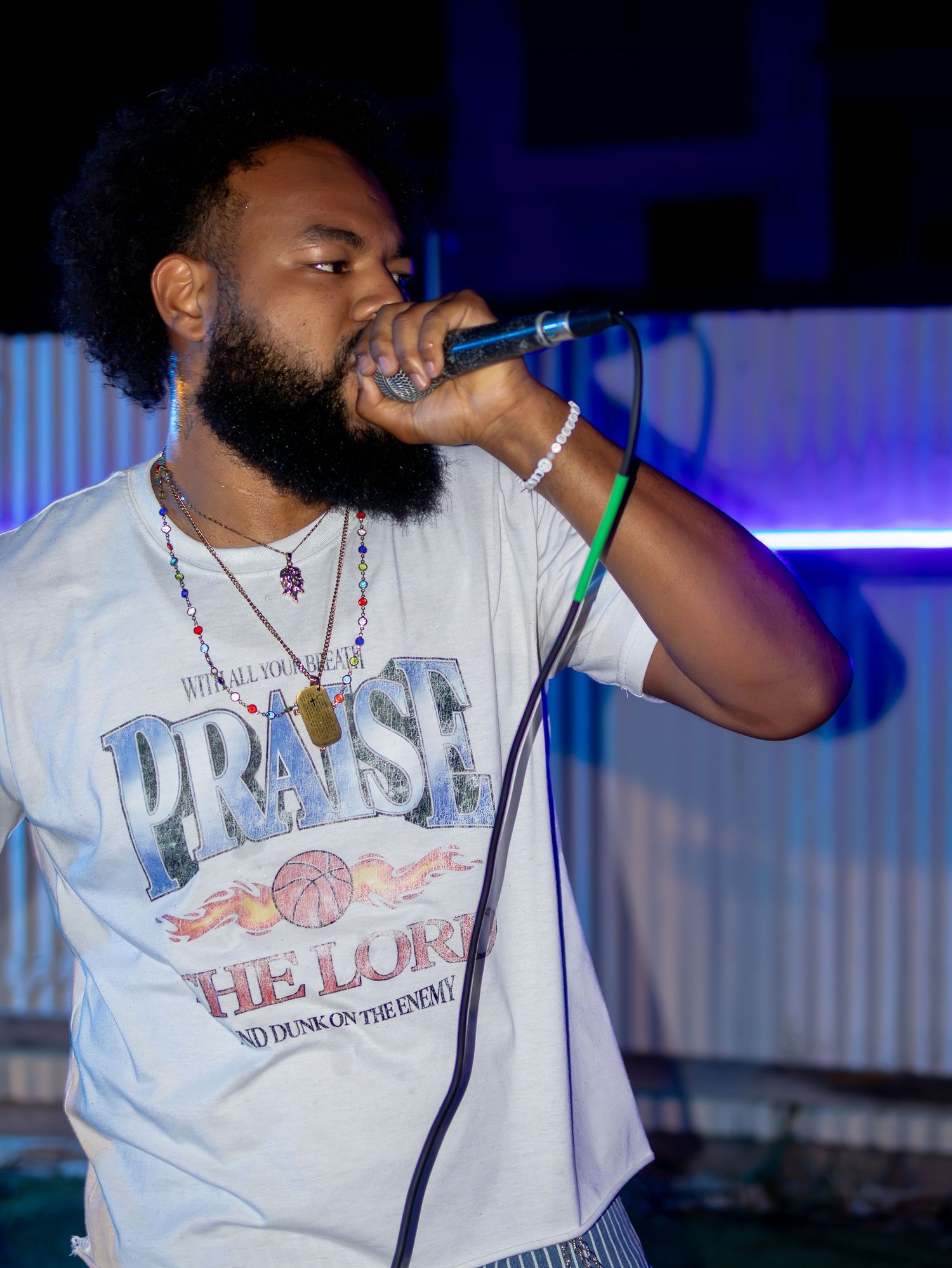 Performer in white graphic tee singing into microphone with dramatic lighting effects.