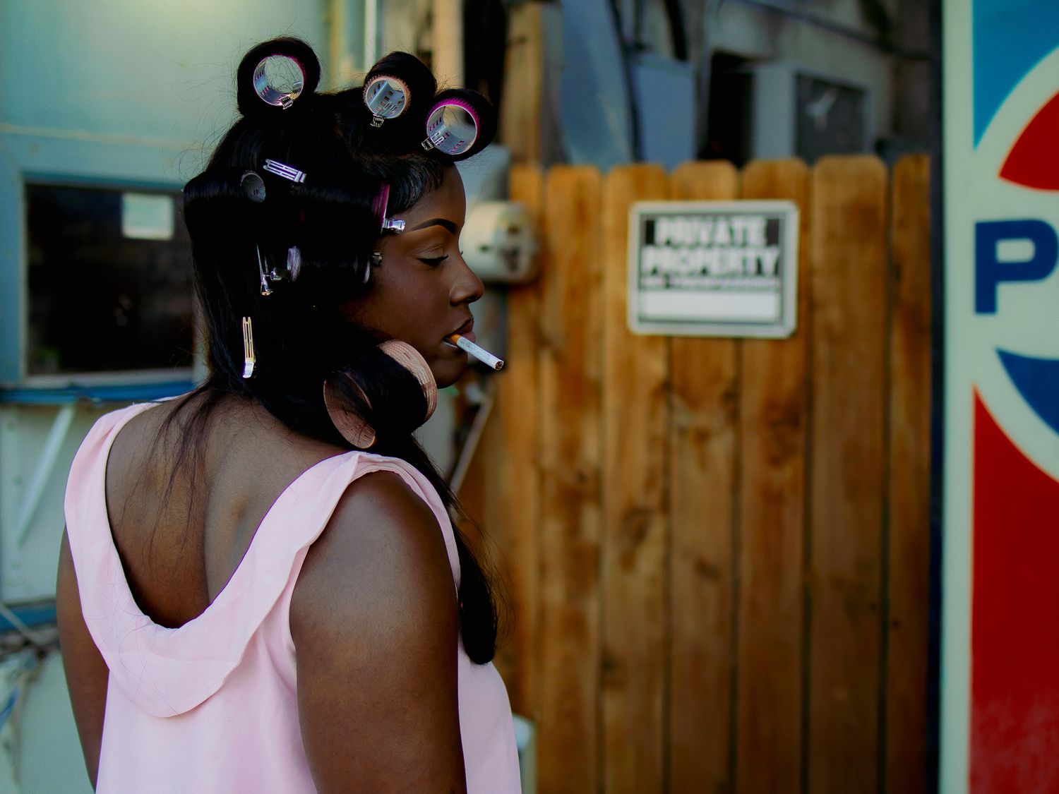 Fashion model wearing pink tank top with hair in black and pink curlers shown from behind.