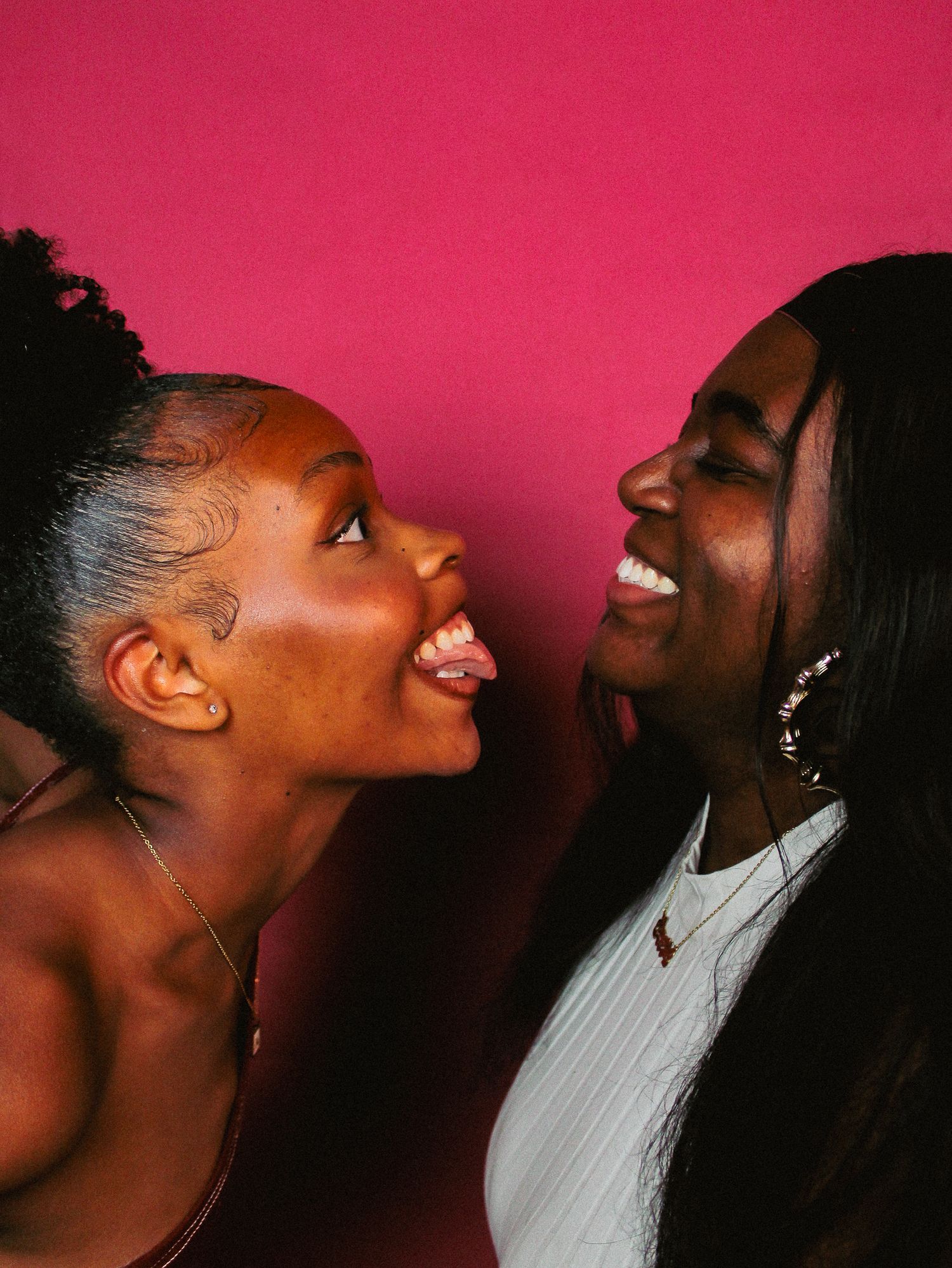 Candid series showing two friends sharing laughter and joy against pink background.