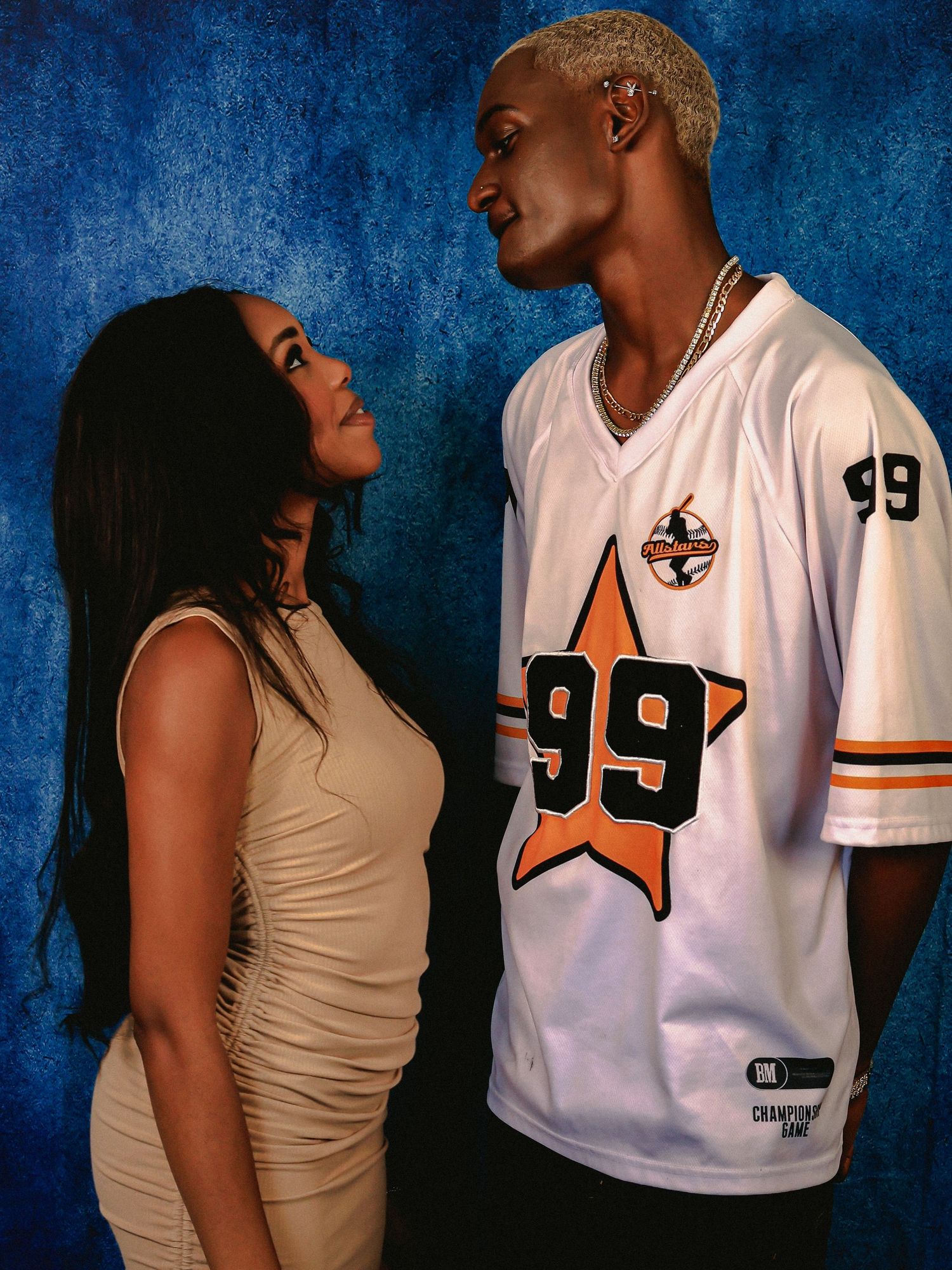Couple in contrasting outfits pose against blue studio backdrop.