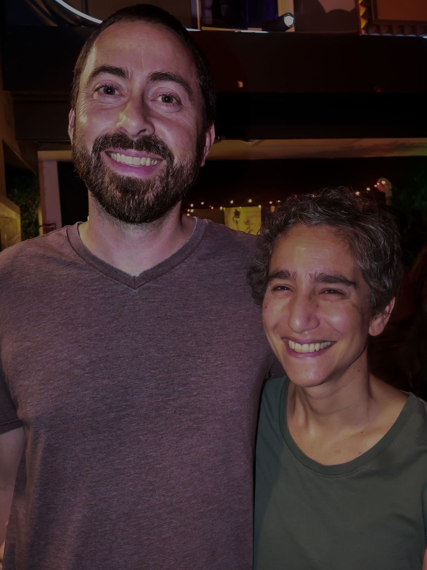 Two people posing together and smiling at a dimly lit event.