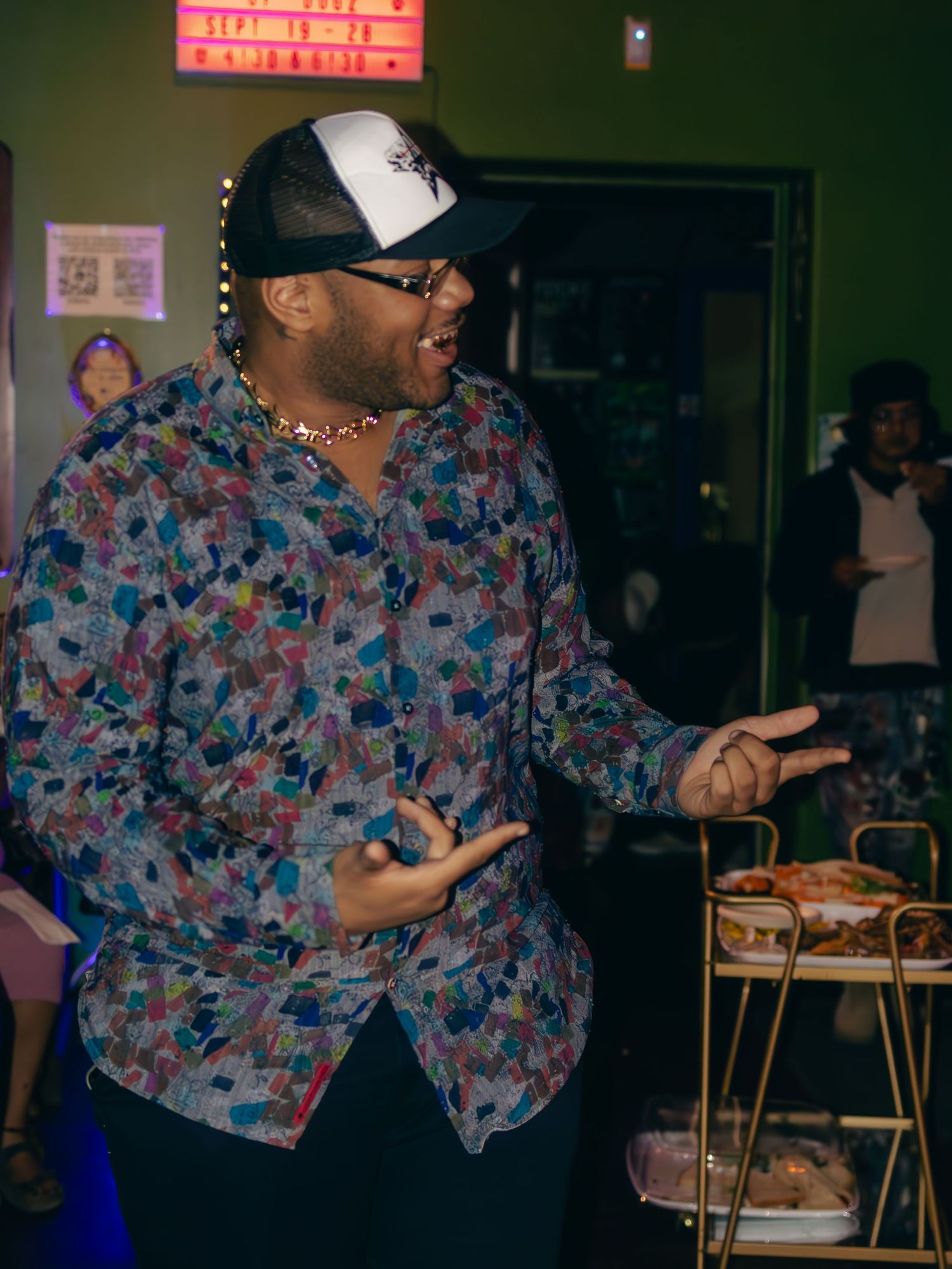 Performer in floral shirt and baseball cap entertaining crowd at nightclub venue.