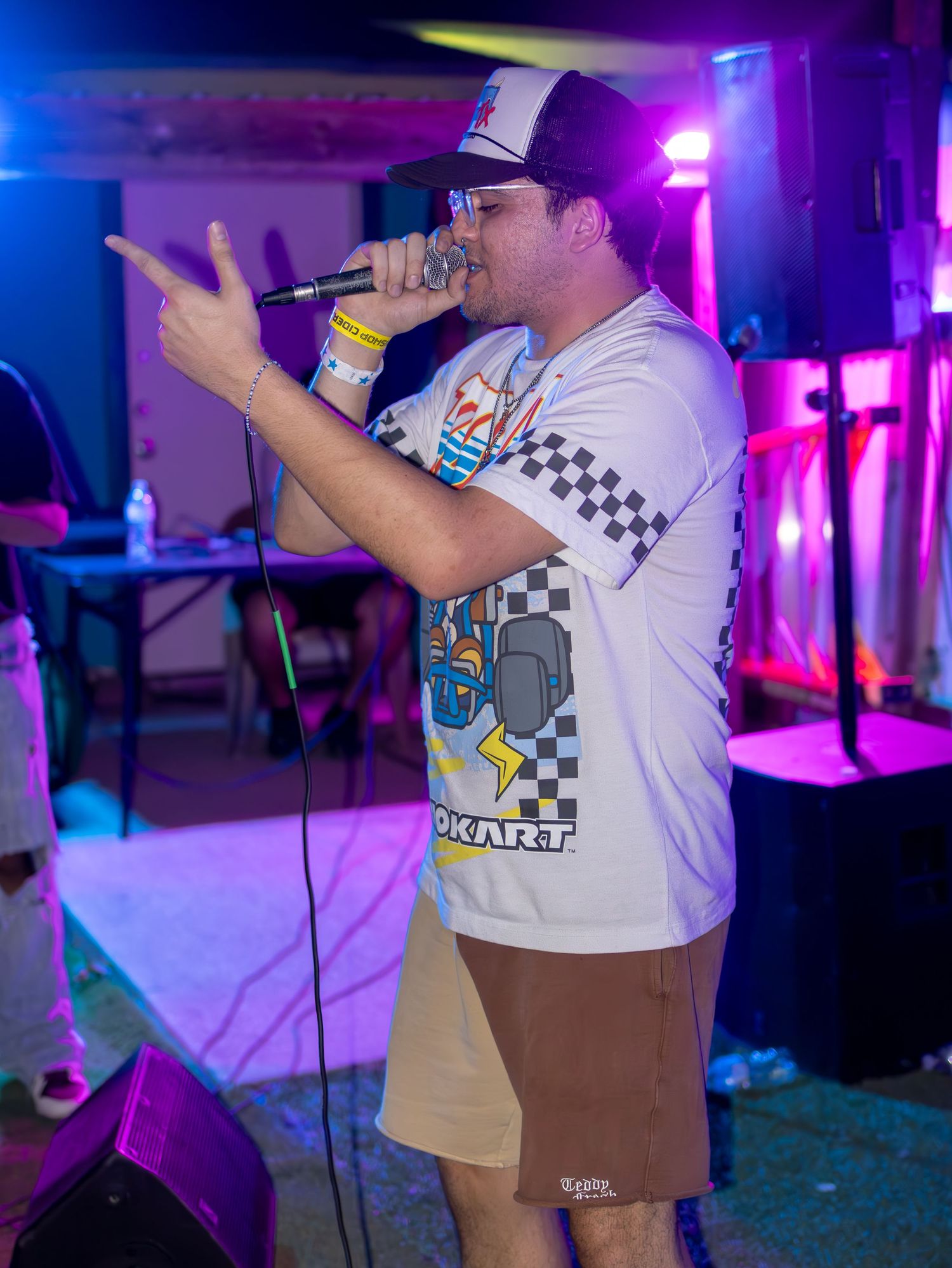 Performer in white Mario Kart t-shirt singing on stage with colorful purple and blue lighting.