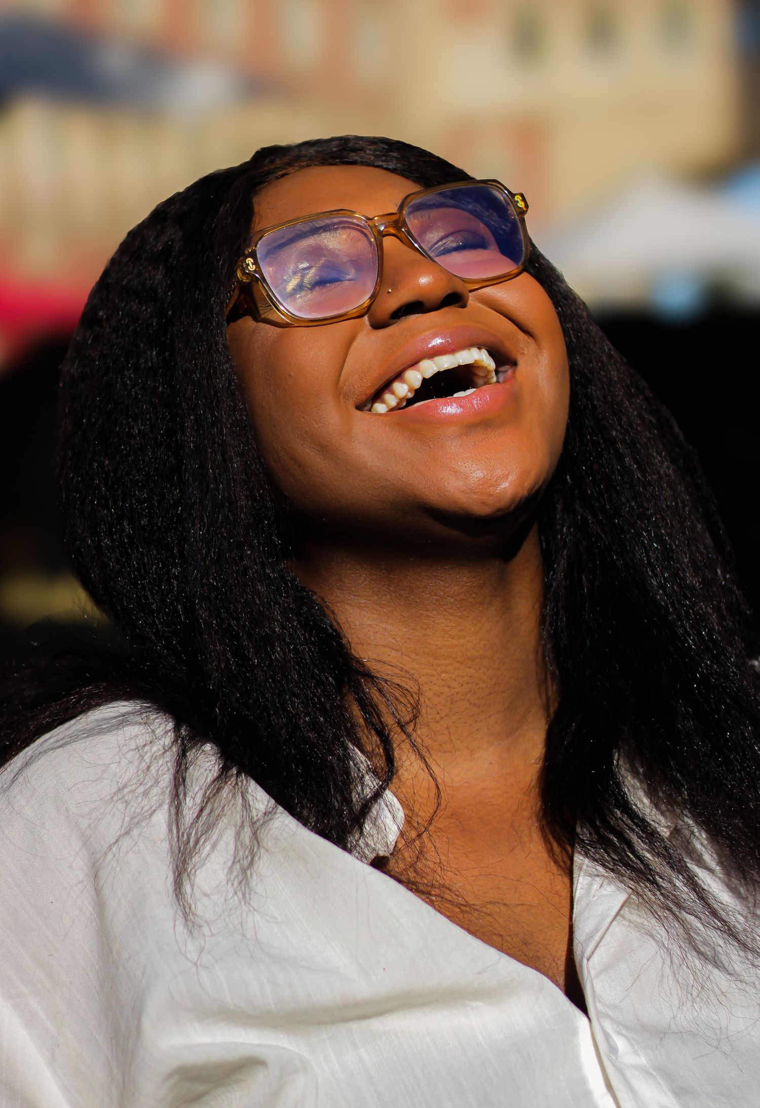 A joyful expression captured in natural lighting while wearing glasses and a white top.