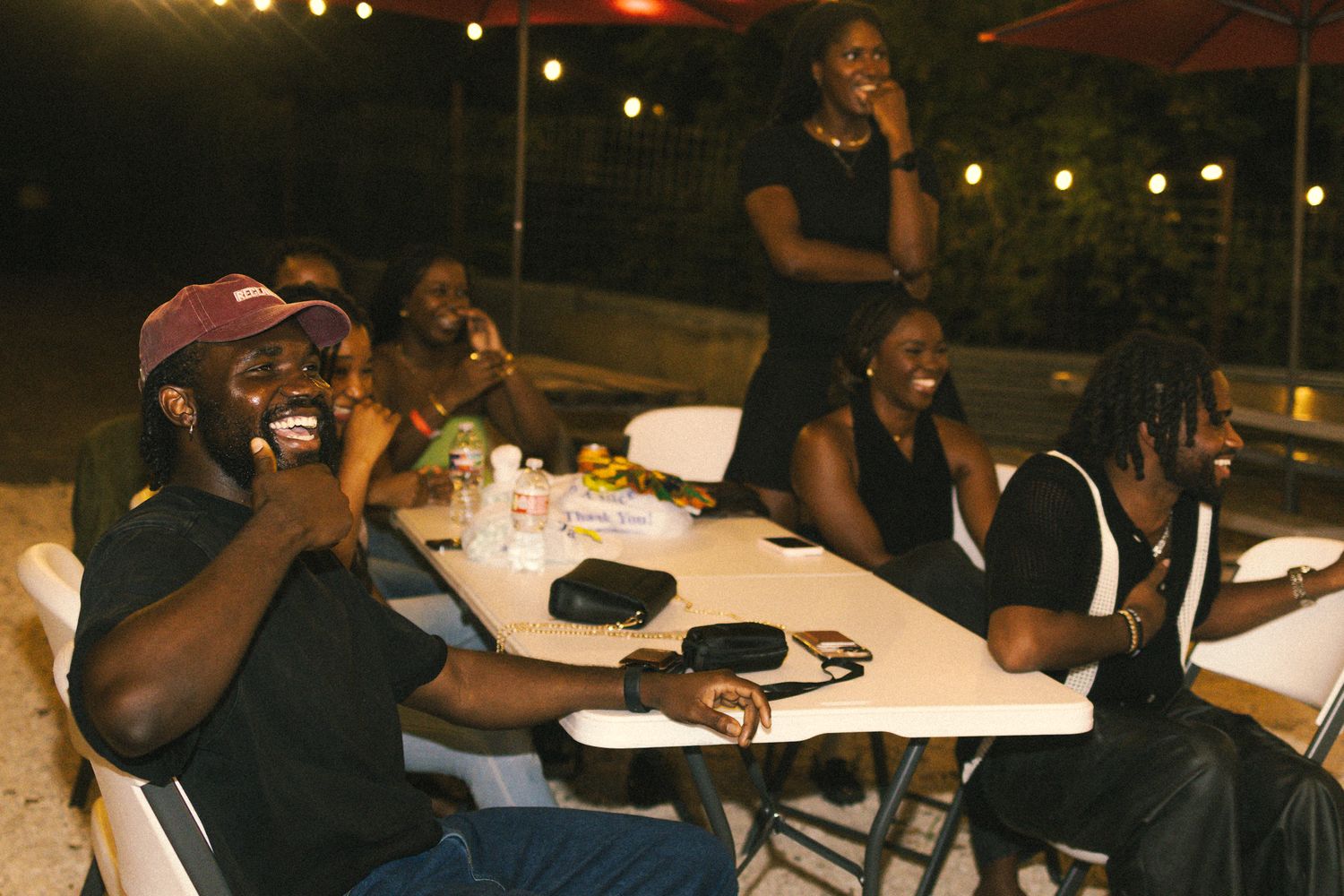 Nighttime social gathering with people seated at outdoor tables under ambient lighting.