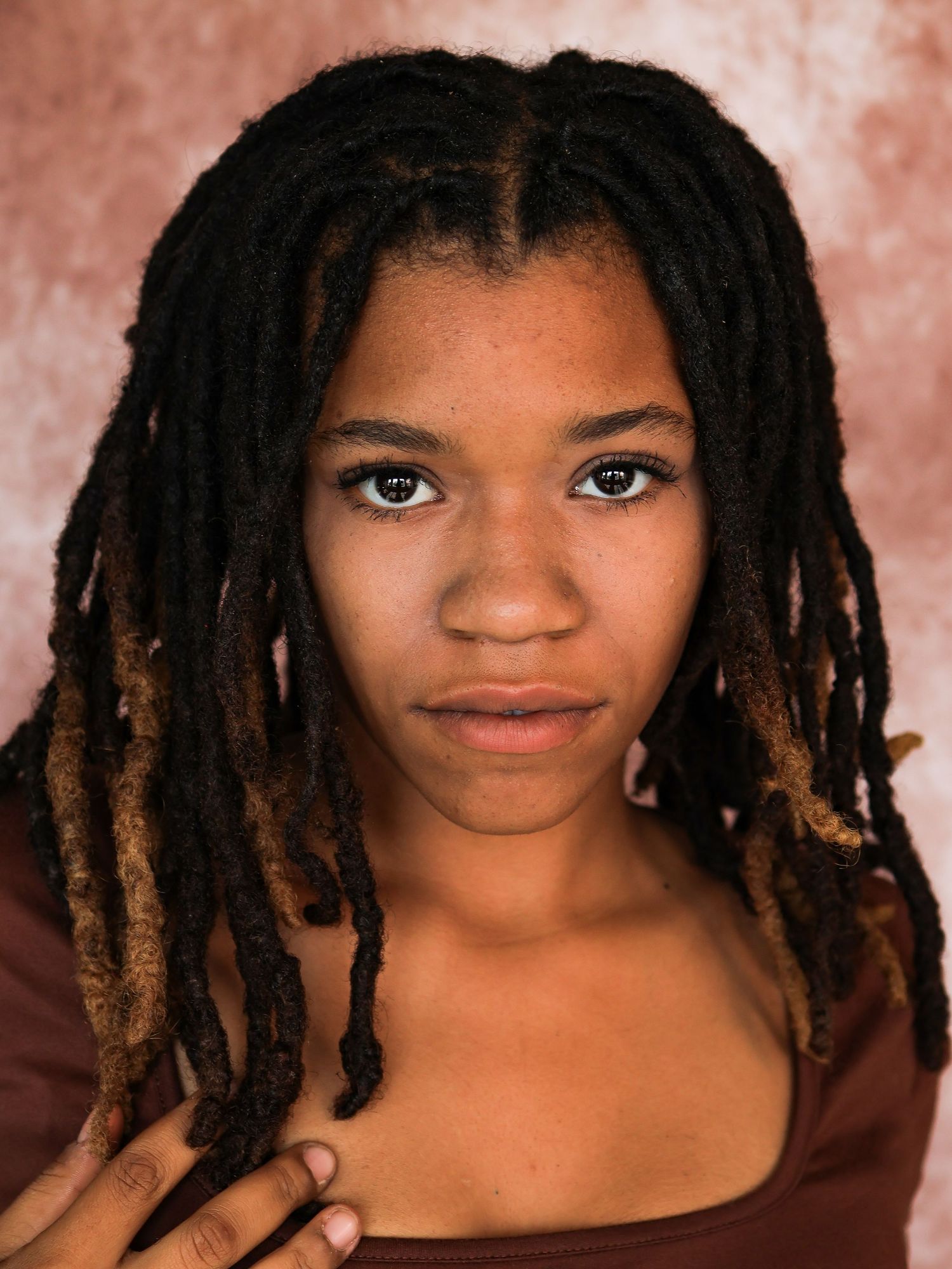Expressive portrait series showcasing natural hairstyle and warm smile against mottled brown background.