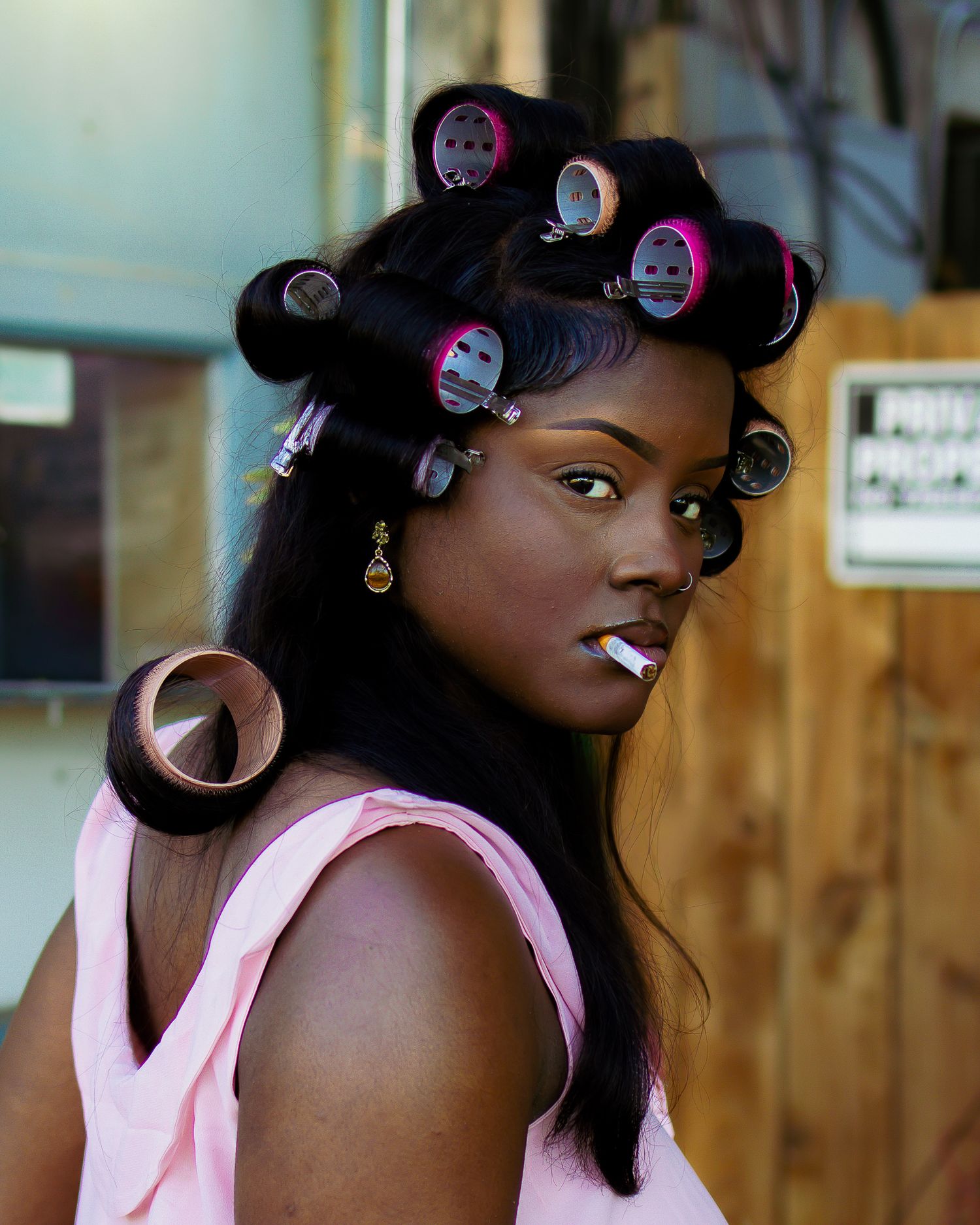 Portrait showing hair in rollers while wearing pink tank top against wooden background.