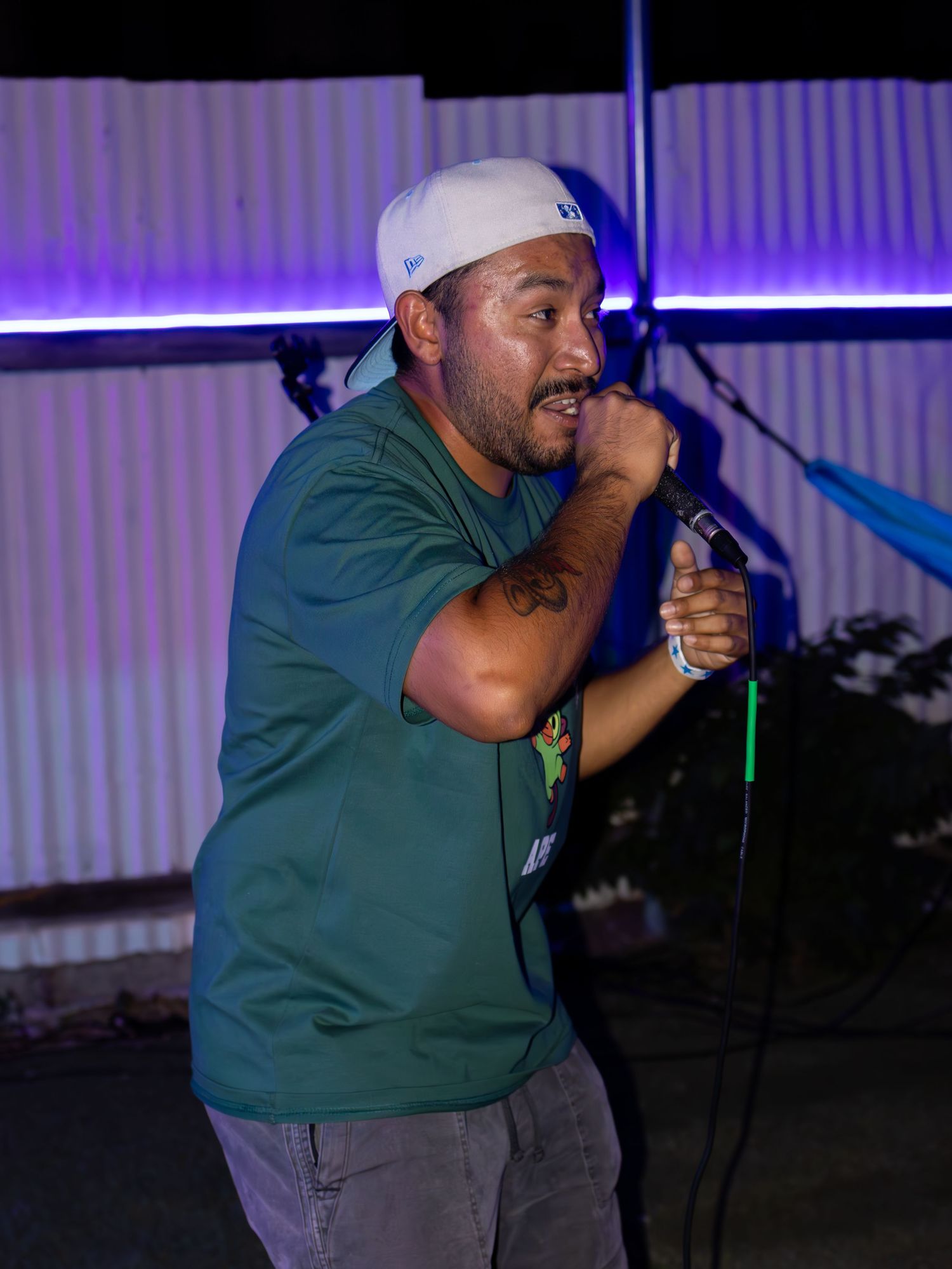 Performer in white cap and green shirt holds water bottle while performing on stage.