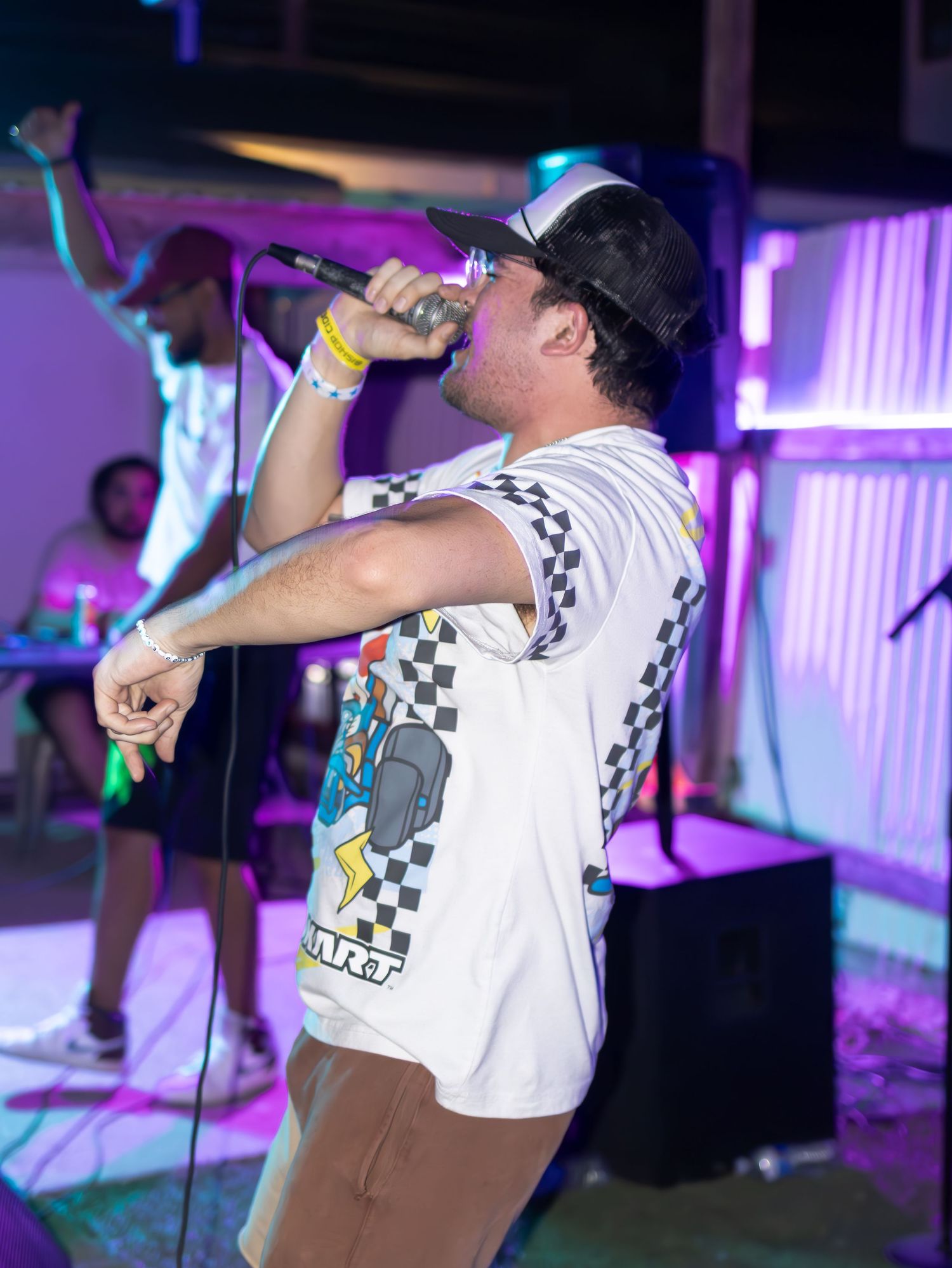 Performer in Mario Kart t-shirt singing passionately under multicolored stage lights.