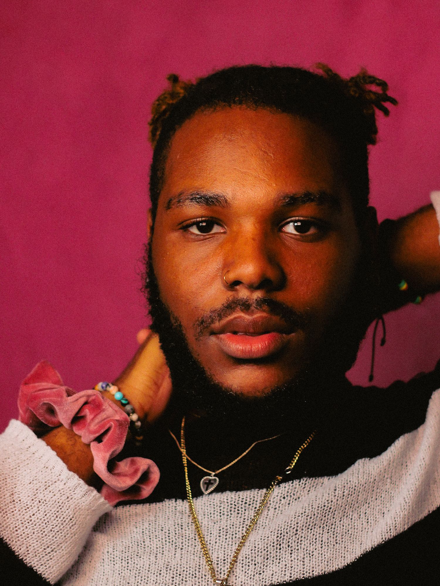 Expressive portrait with pink accent and gray sweater against red backdrop.