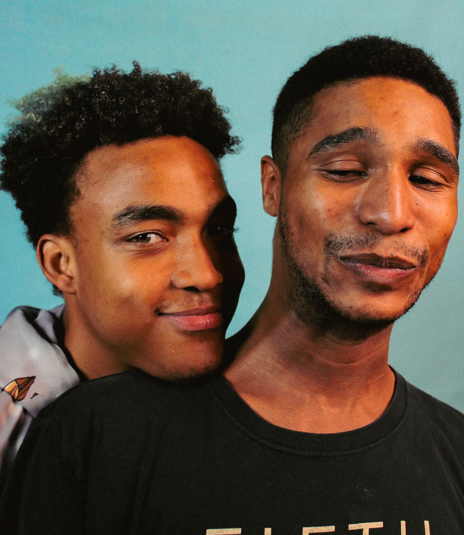Two friends sharing a lighthearted moment while posing against a blue backdrop.