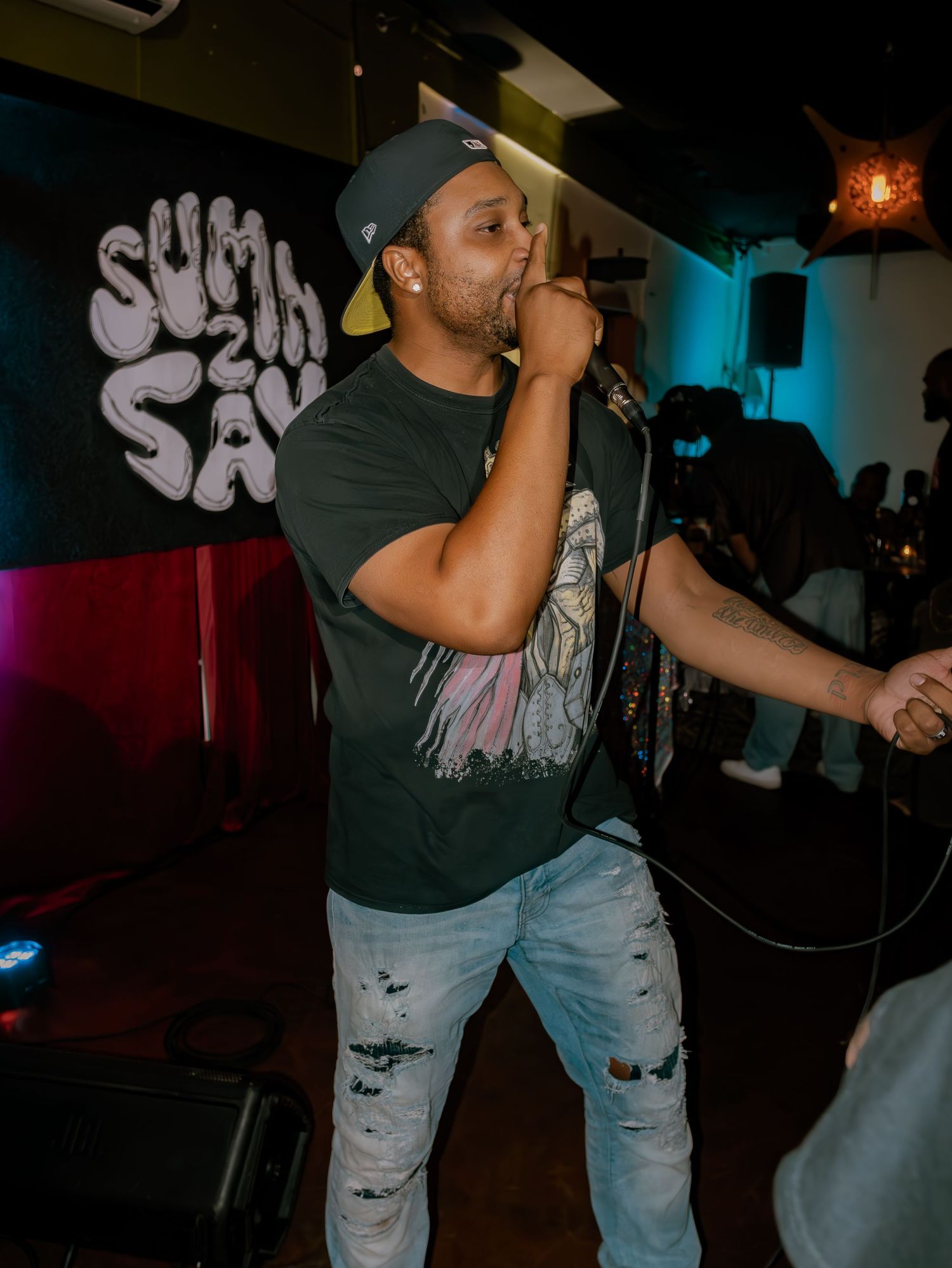 Performer in distressed denim and dark shirt delivers energetic performance in club setting.