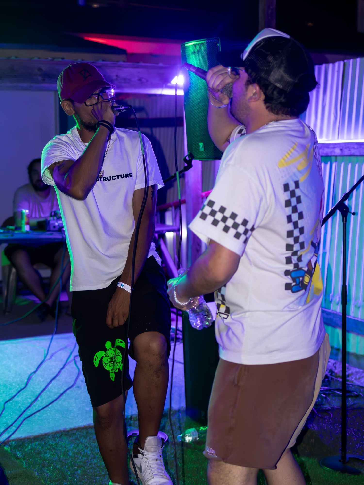 Musicians performing on stage with colorful lighting and white t-shirts with checkered patterns.