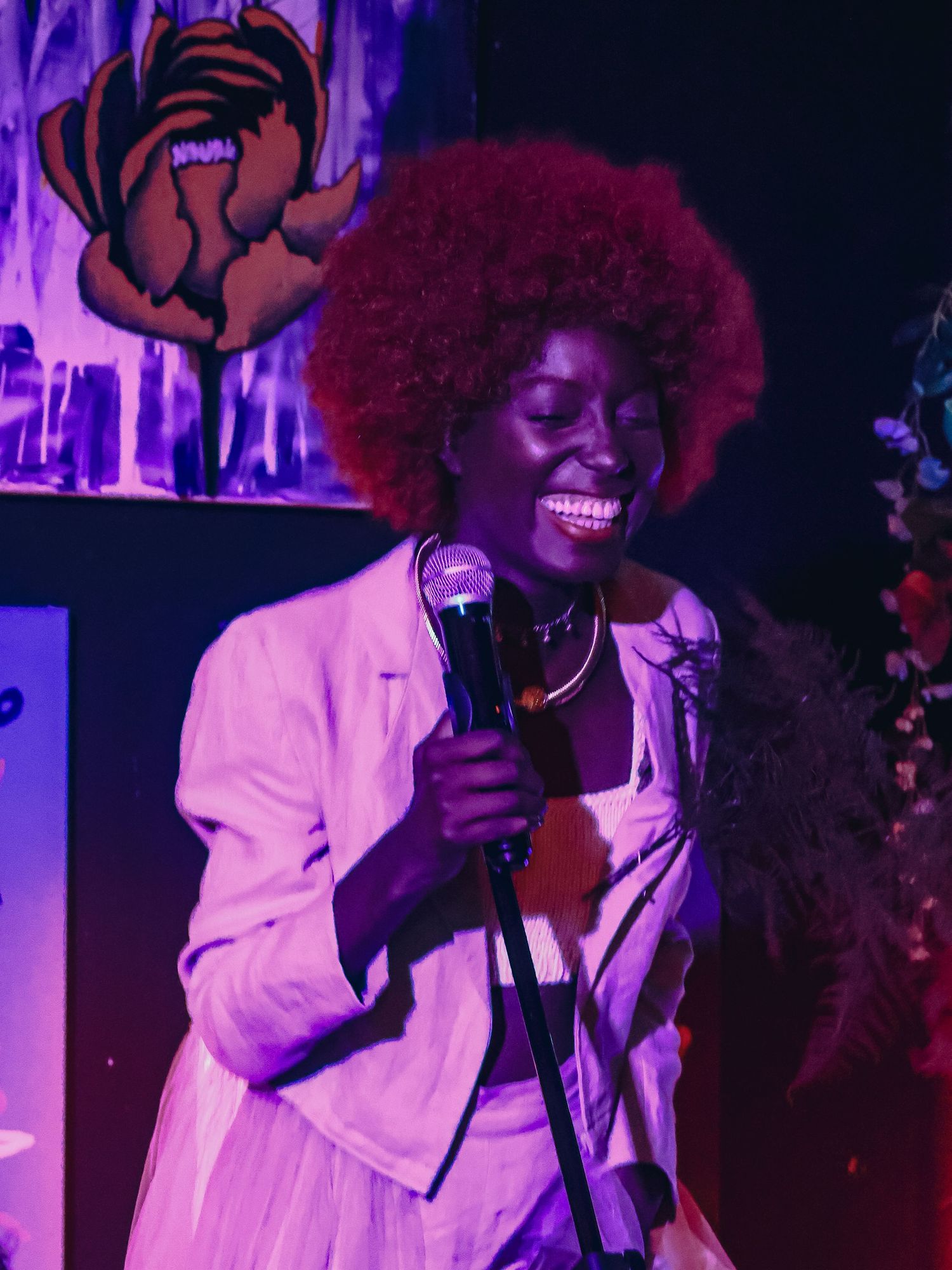 A performer in a white dress sings on stage under purple lighting during a show.