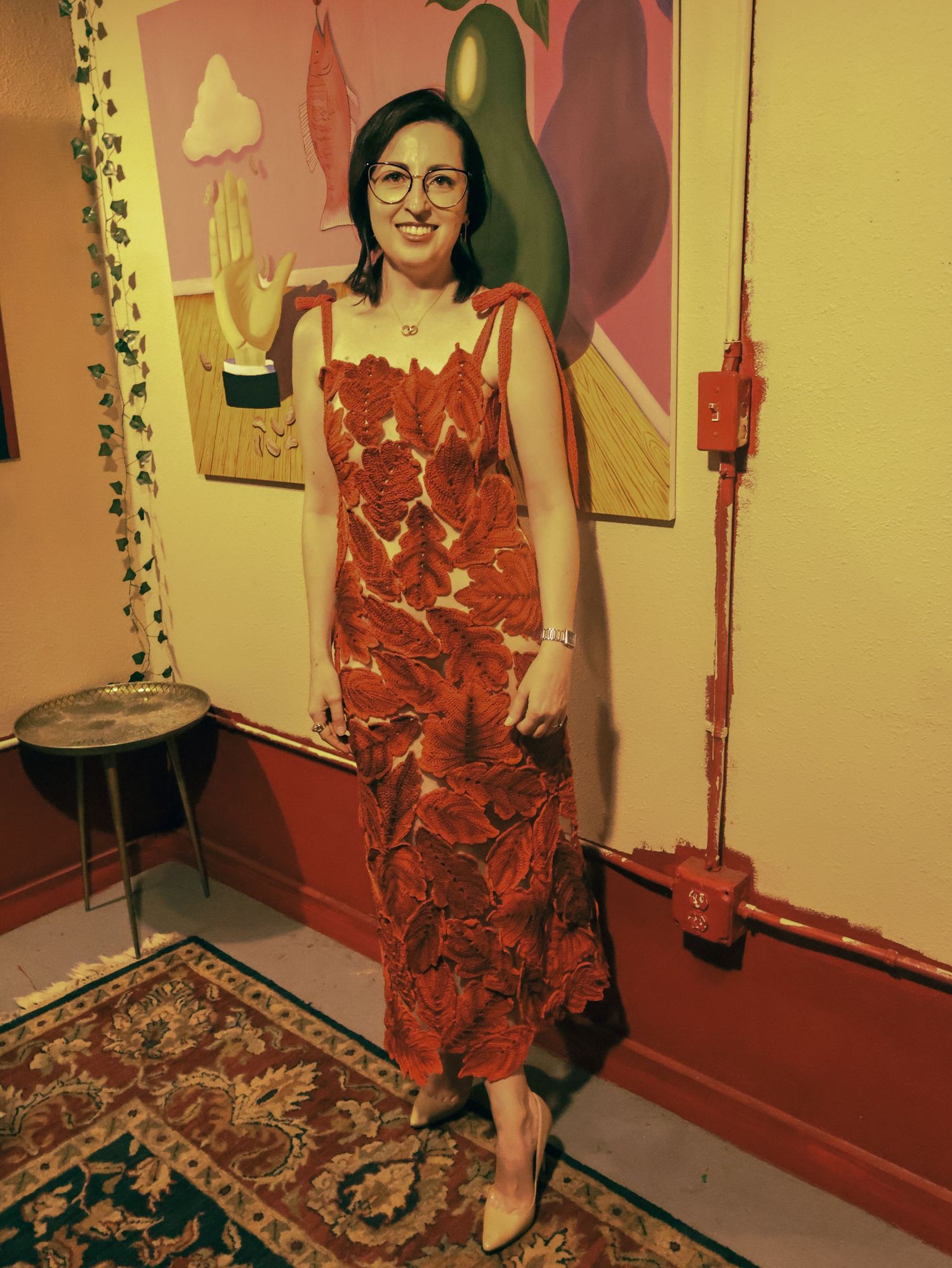 A red lace dress is modeled in a room with decorative wall art and a patterned rug.