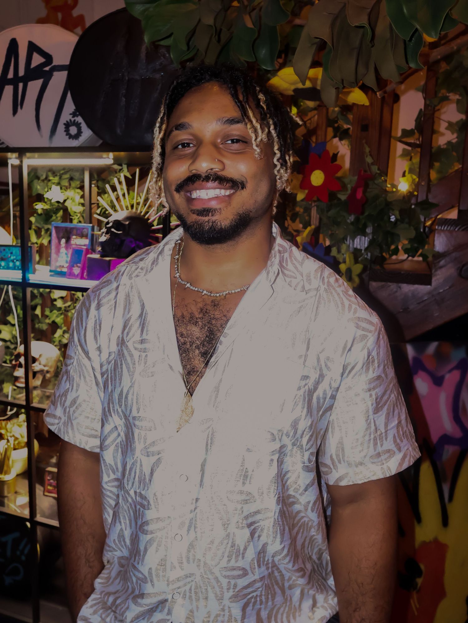 Person in white patterned shirt smiling at a party venue with colorful lighting.