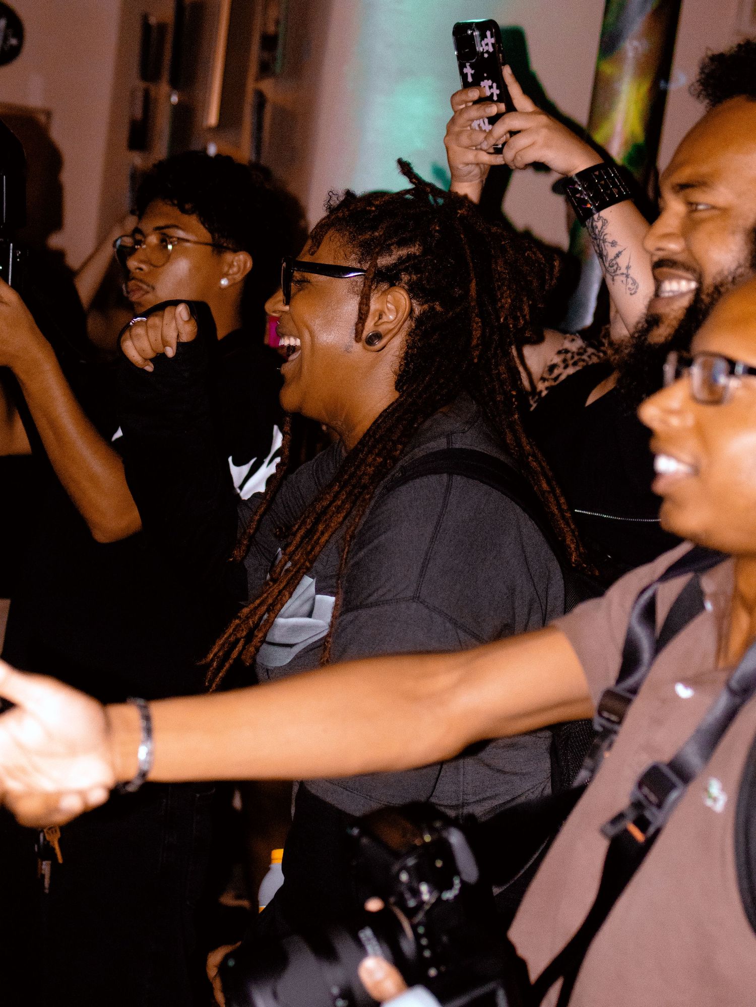 Crowd at a concert holding phones and dancing with arms raised in dimly lit venue.