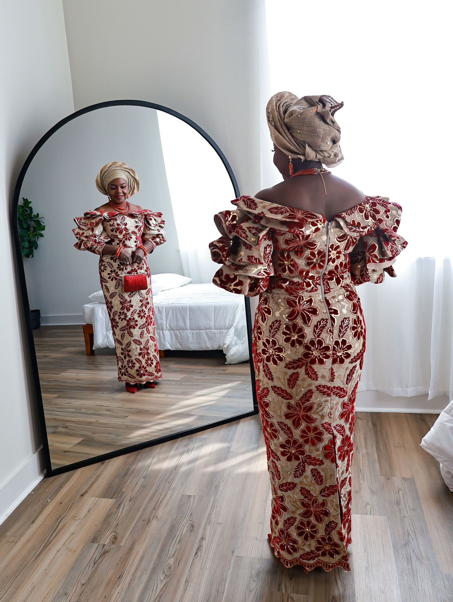 A person in a floral red and white dress poses in front of a full-length mirror in a bright room.
