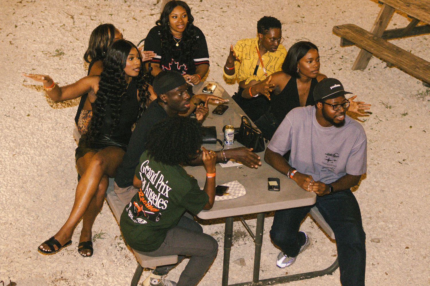 Group of people sitting at tables in a casual outdoor setting during evening hours.
