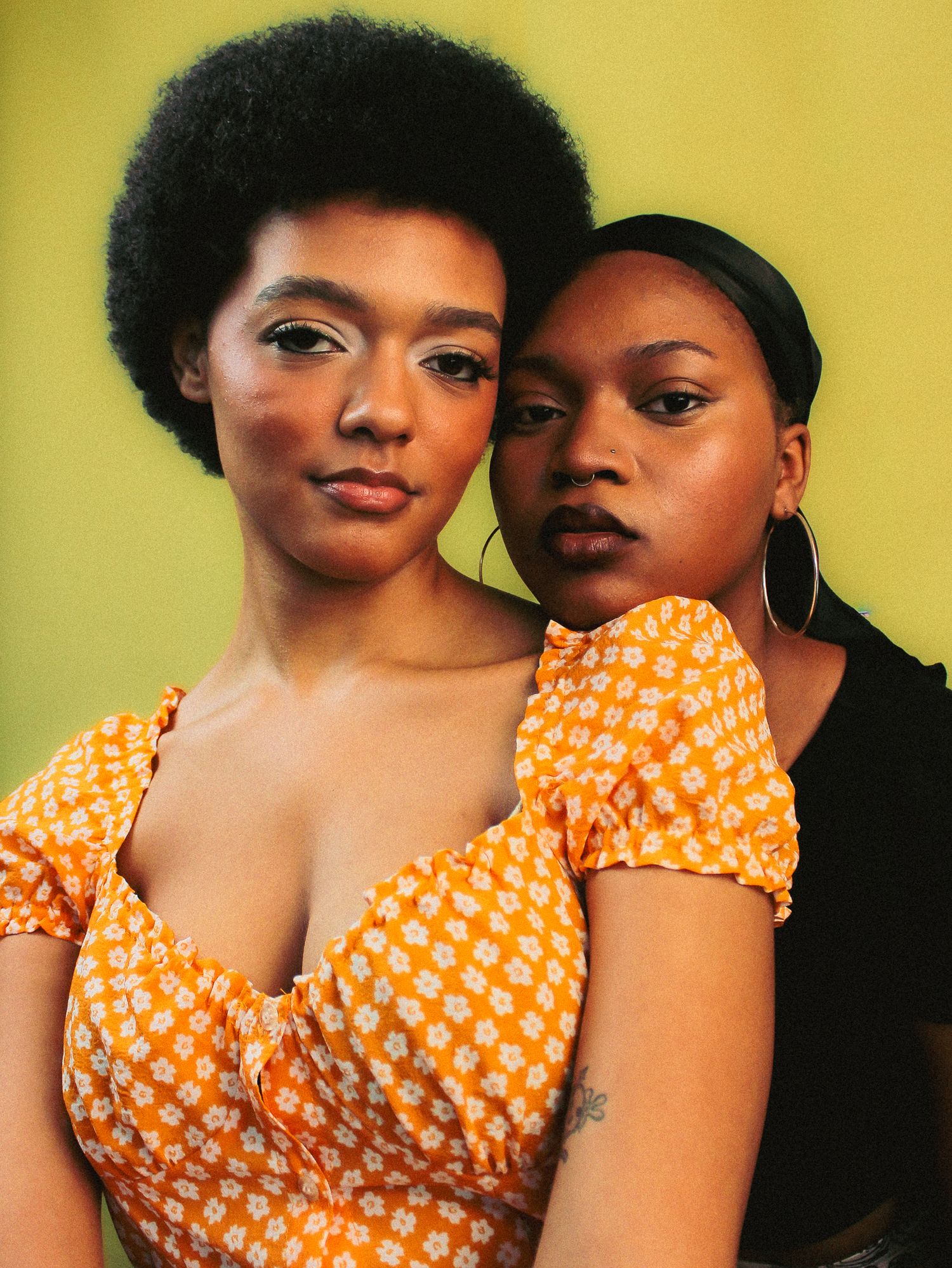 Two people in orange polka dot tops pose together against a yellow background.