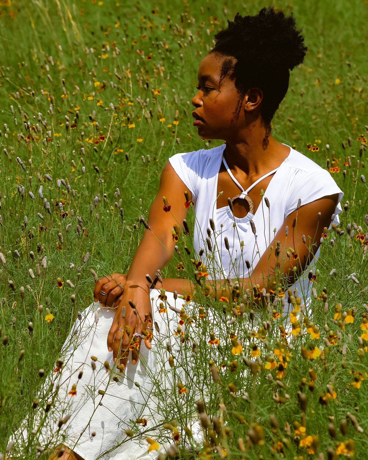 Side profile portrait amid flowering meadow wearing white summer attire.