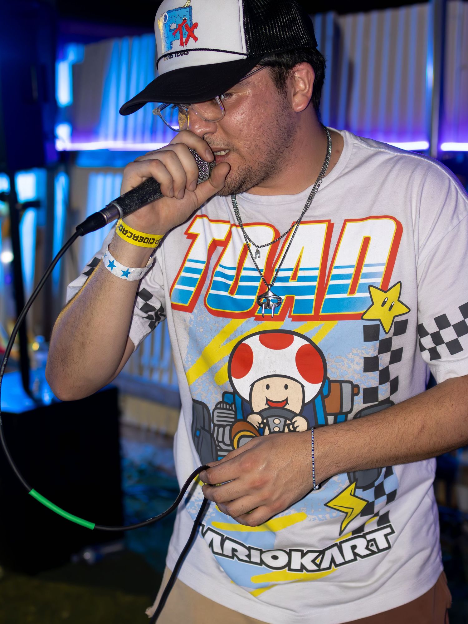 Performer in Mario Kart t-shirt singing into microphone with neon lights behind.