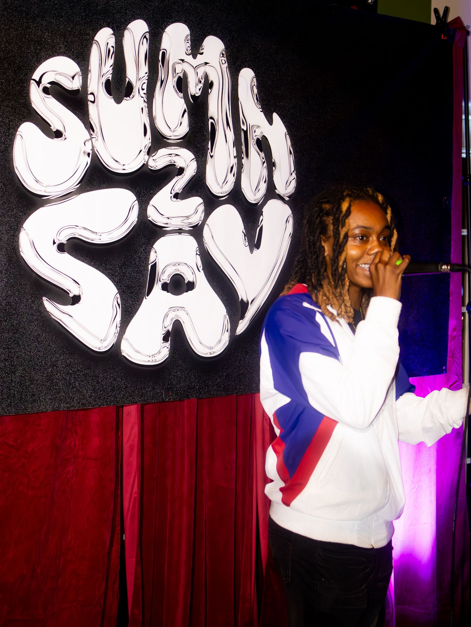 Artist performing in front of 'South Sav' sign wearing white and blue athletic jacket.