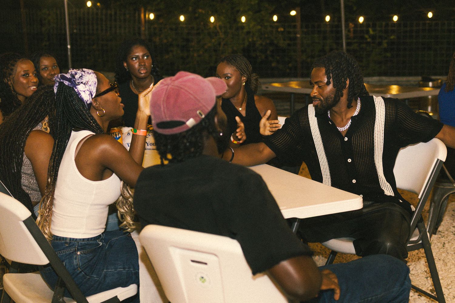 Crowd seated at white tables during outdoor nighttime social gathering.
