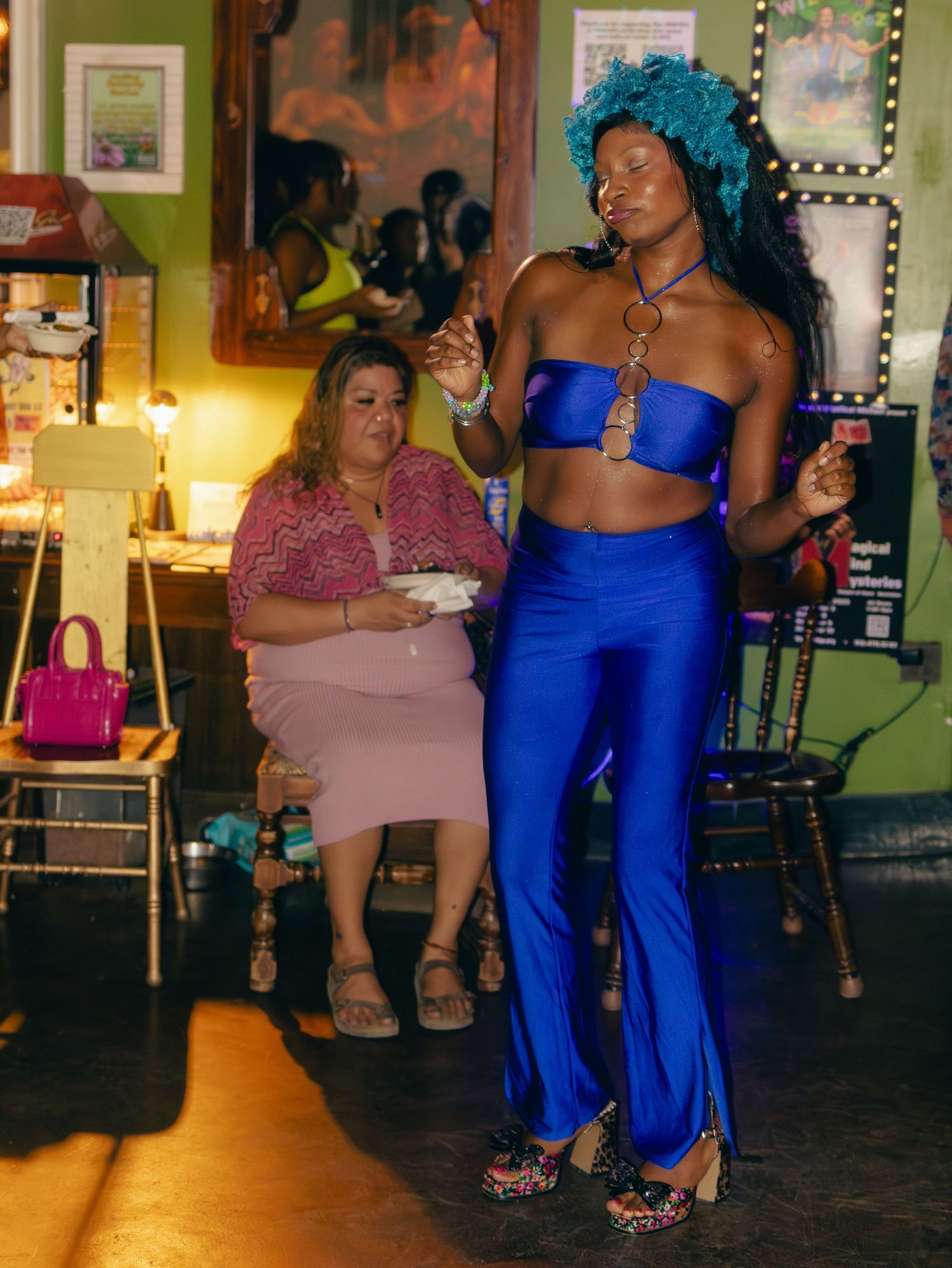 Two partygoers enjoying a night out at a club, one wearing a bright blue outfit with turquoise hair and another in pink.