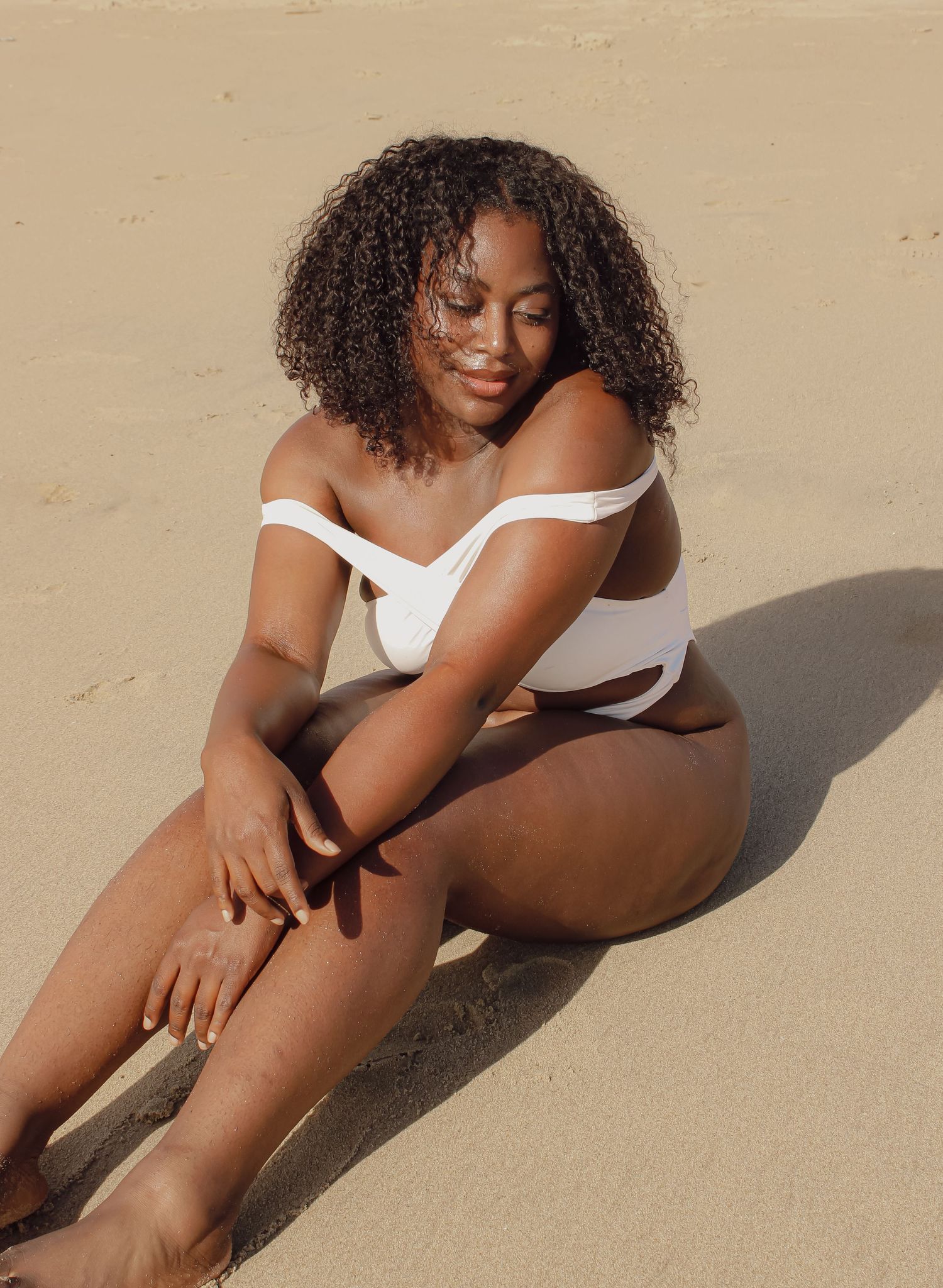 Sunlit beach photography session with white swimwear on sand.