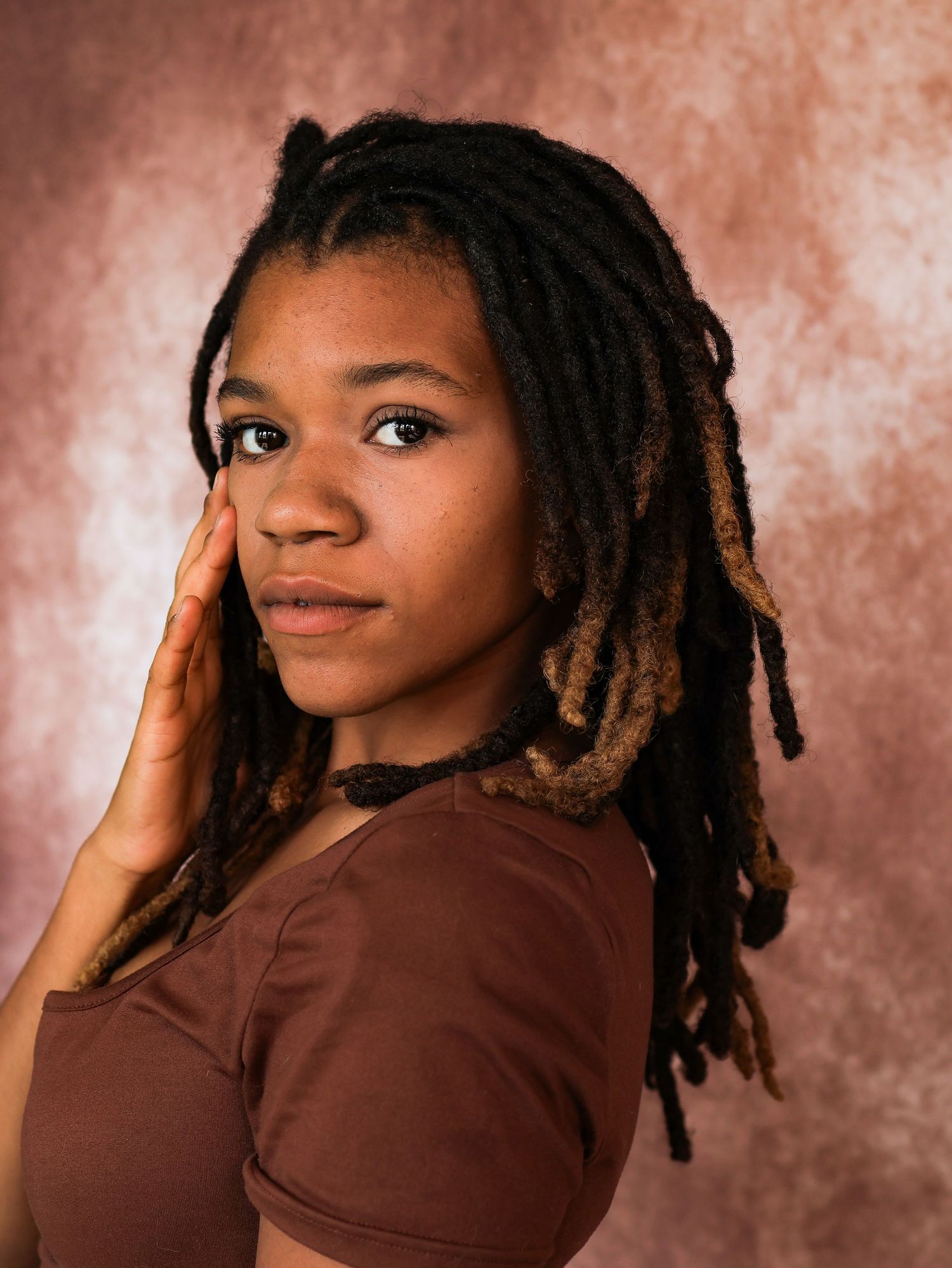 Portrait series with dreadlocks against warm brown studio backdrop.