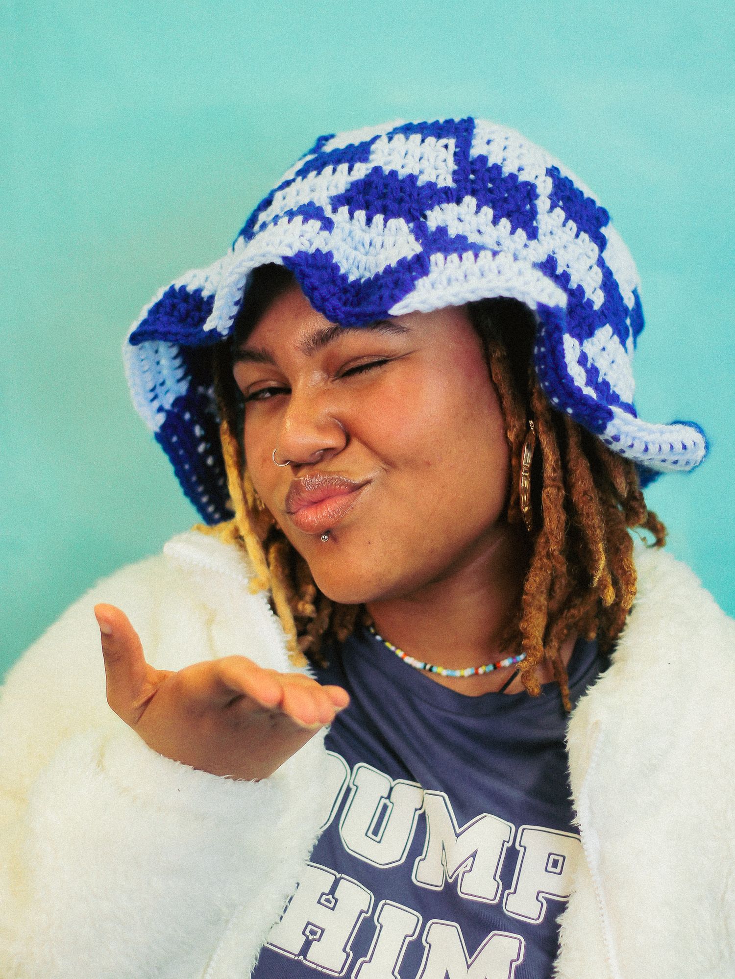 Young woman in blue checkered crochet bucket hat blowing a kiss wearing Dump Him graphic tee.