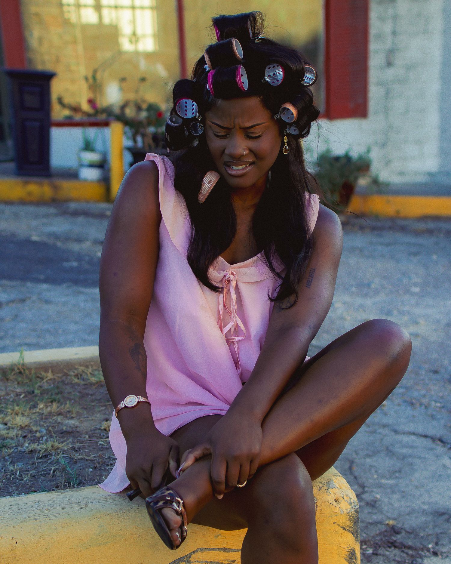 A person with hair rollers sits outdoors in a pink sleeveless top.