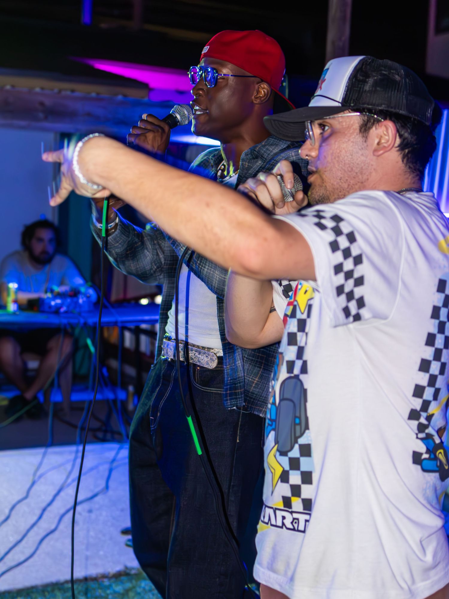 Musicians performing on stage wearing checkered shirts under colorful venue lighting.