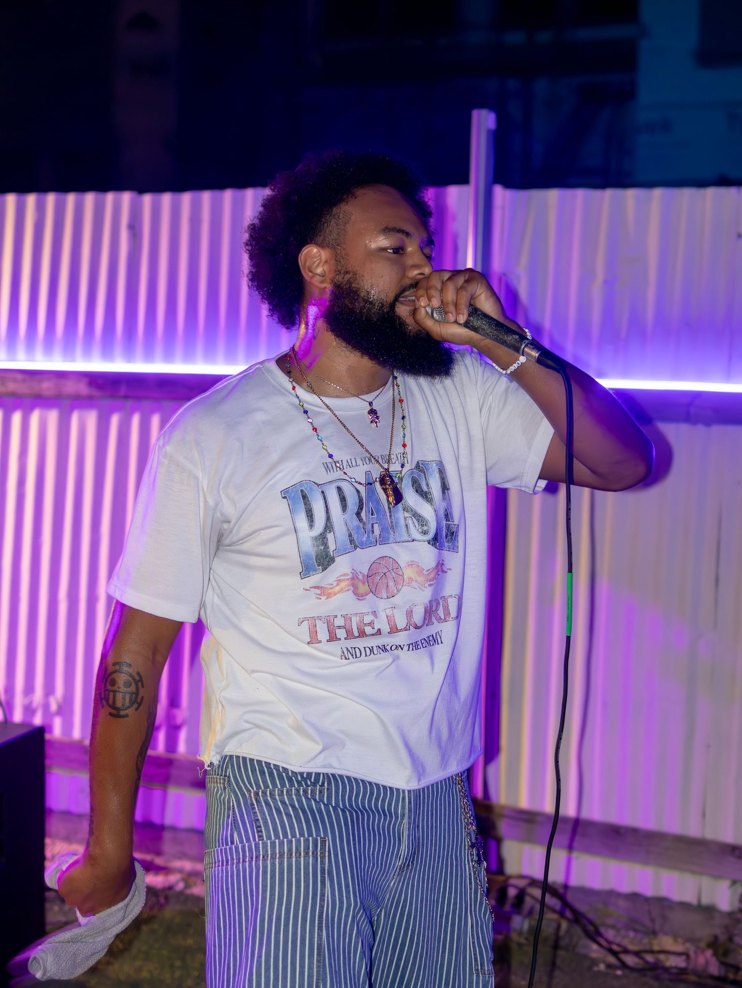 Performer in white t-shirt and striped pants energetically singing on stage with purple lighting.