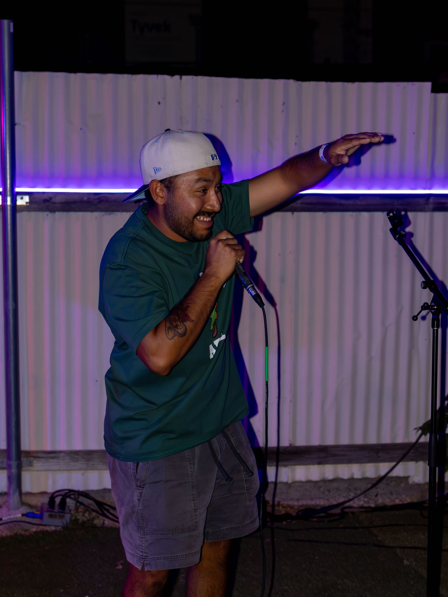 Performer gestures enthusiastically while holding microphone on stage with purple backlit wall.