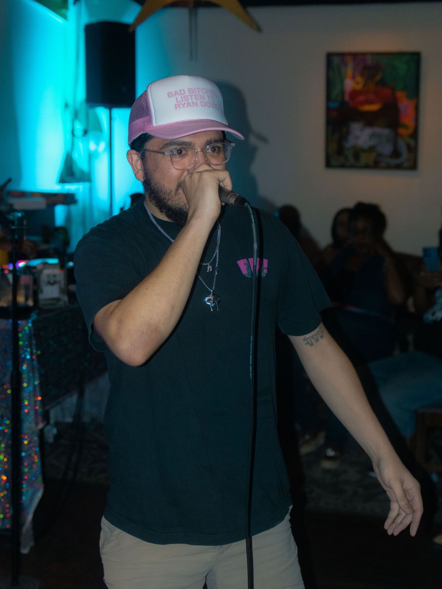 A performer in black clothing and a baseball cap holds a microphone during a live show.