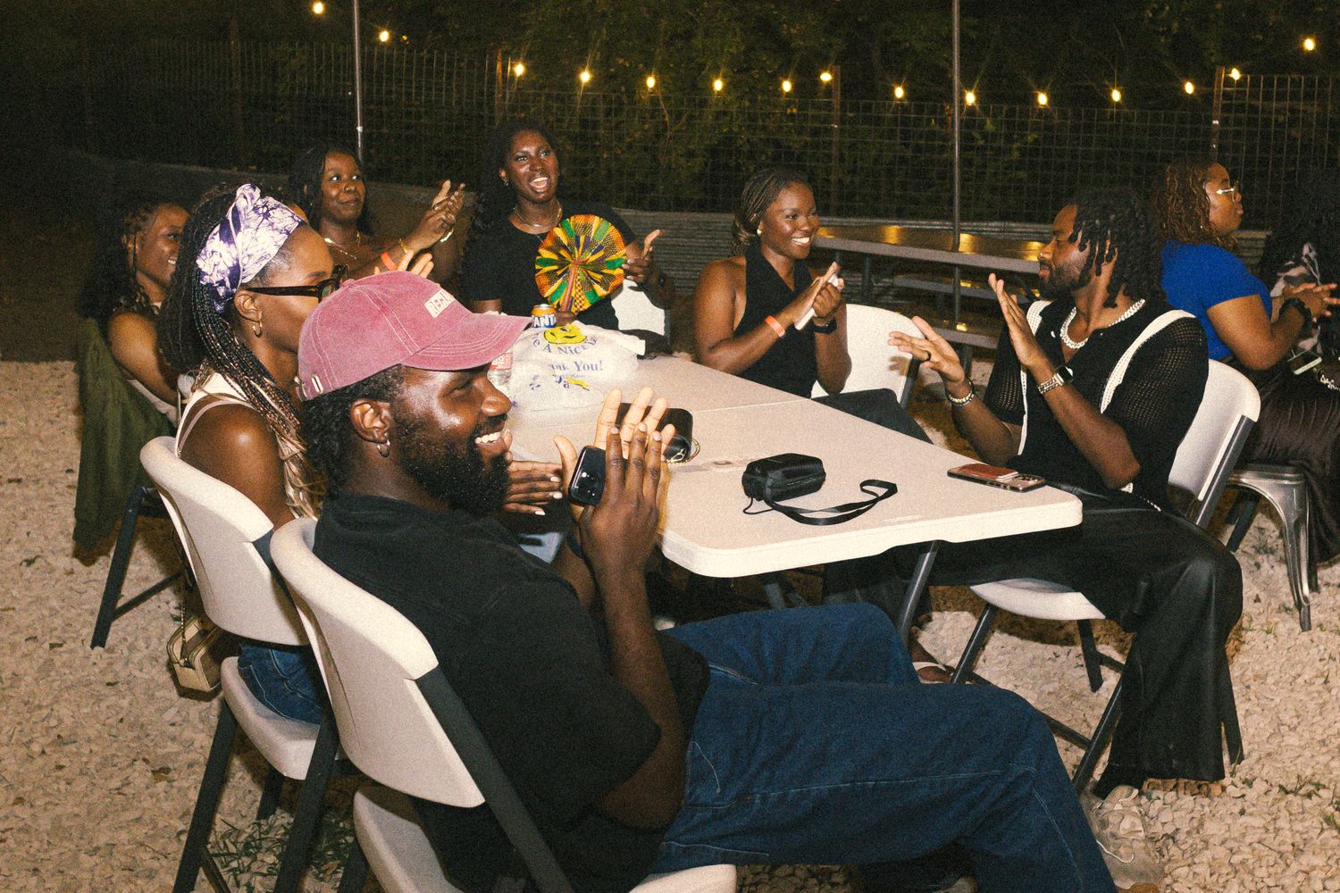 People gathered at outdoor tables under string lights for a nighttime social event.
