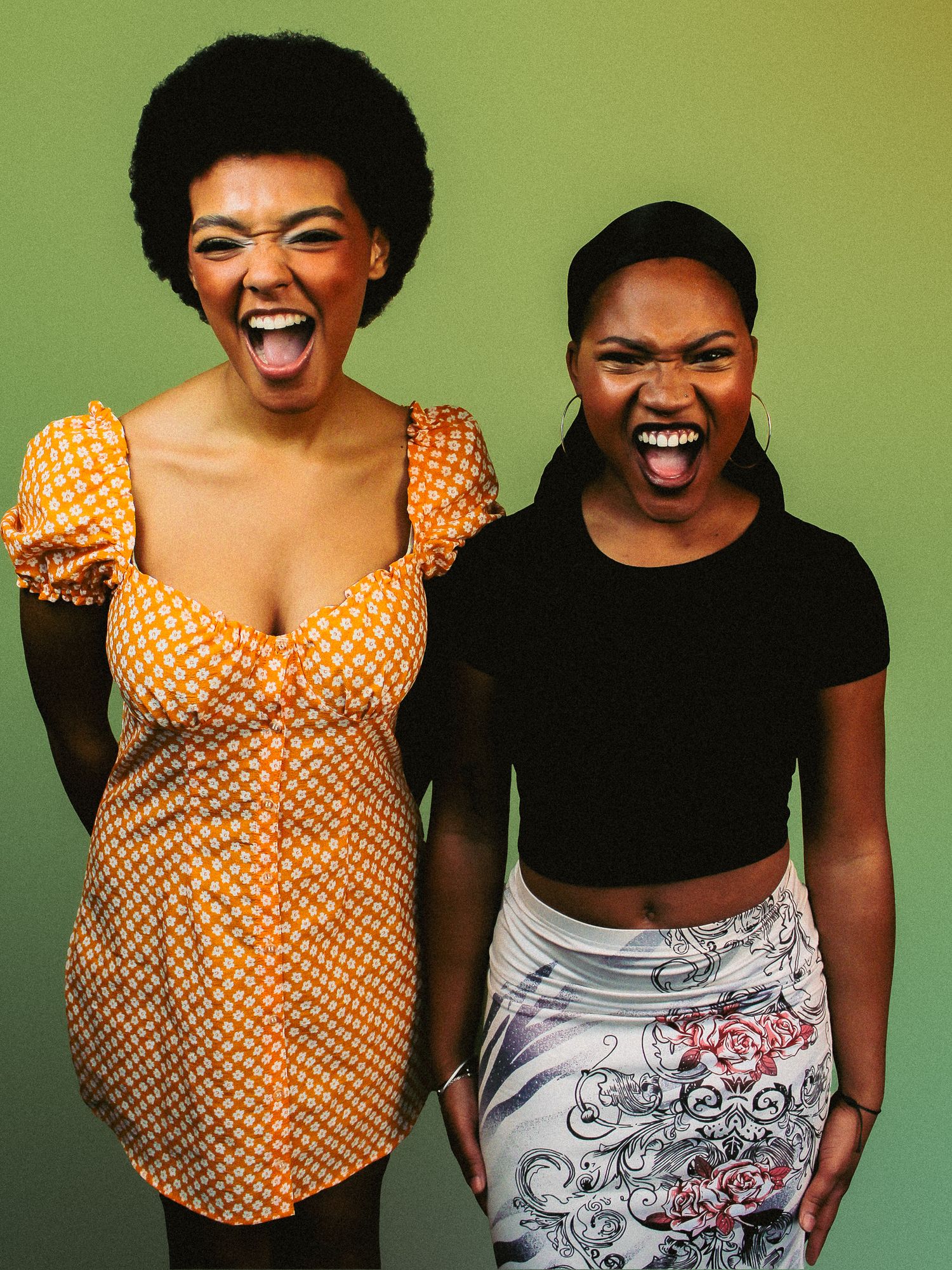 Two young women laughing joyfully together against a vibrant green background.