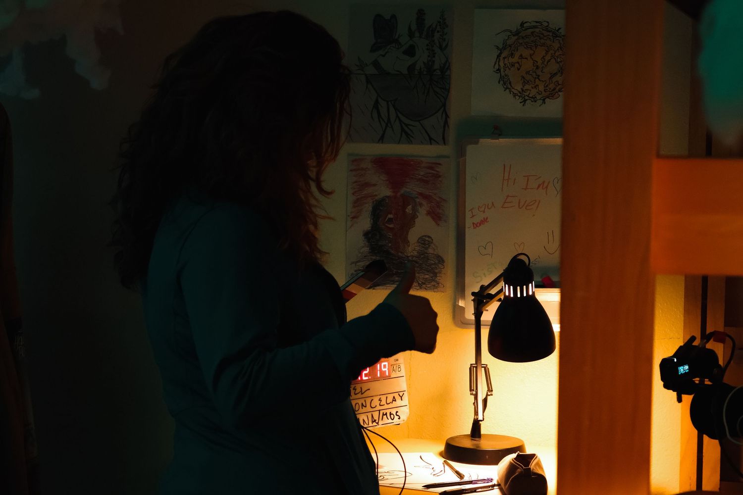 Dark interior film set with dramatic lighting and equipment visible against walls.