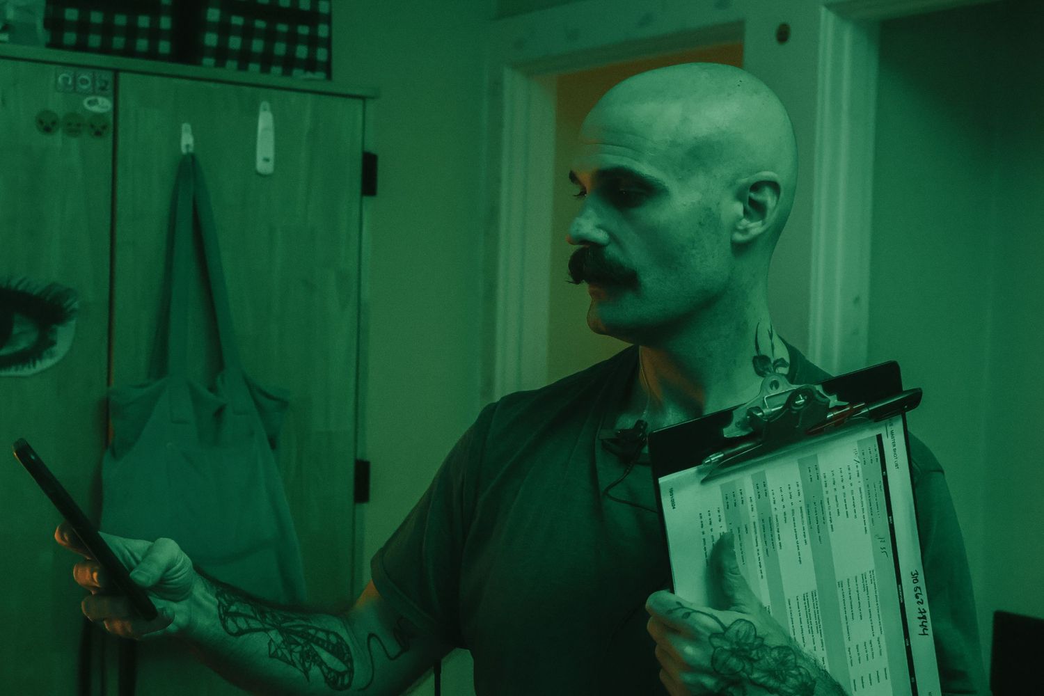 Recording studio scene bathed in green lighting with equipment and papers visible.