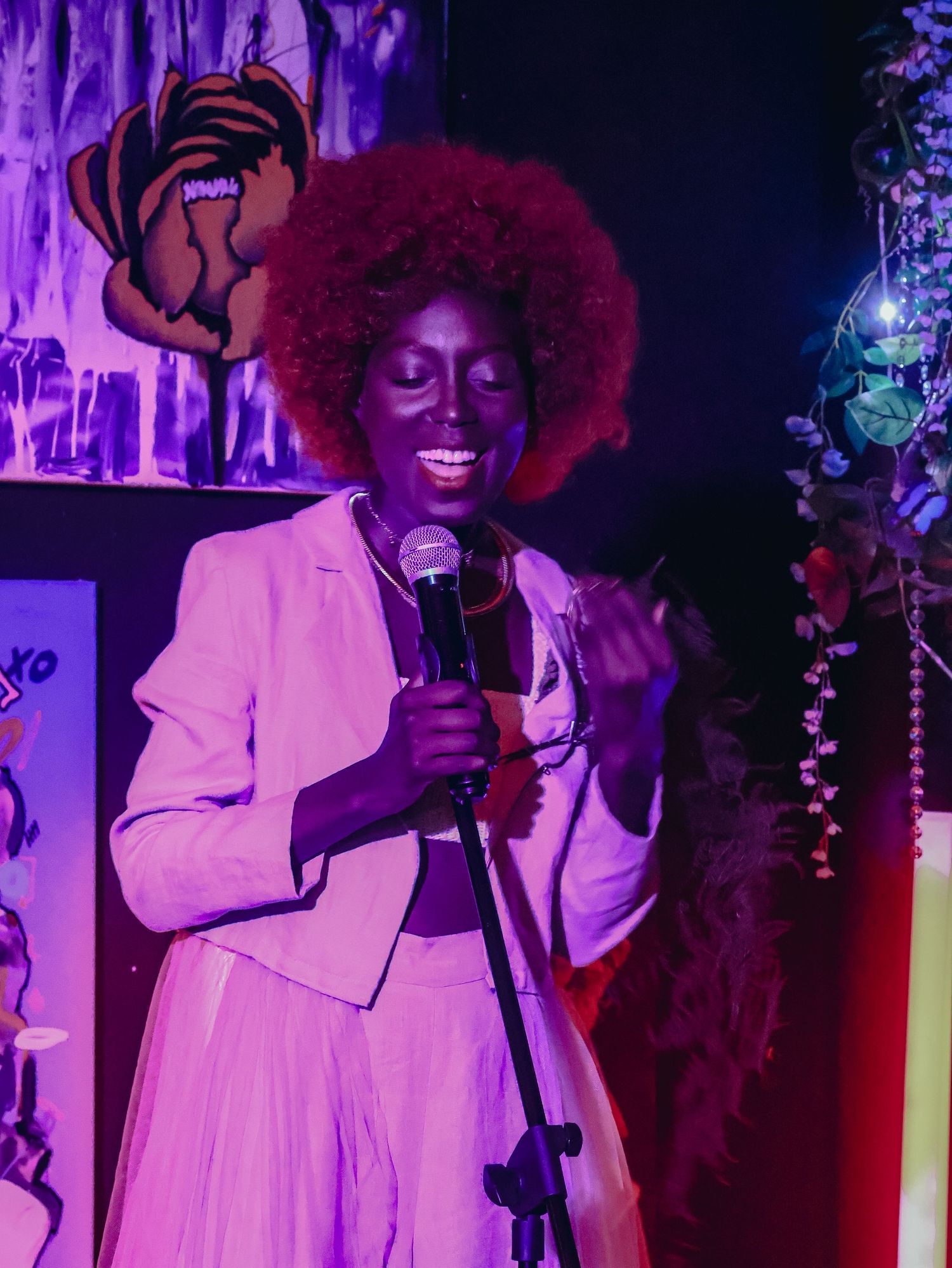 A performer in white holds a microphone while singing under purple stage lights.
